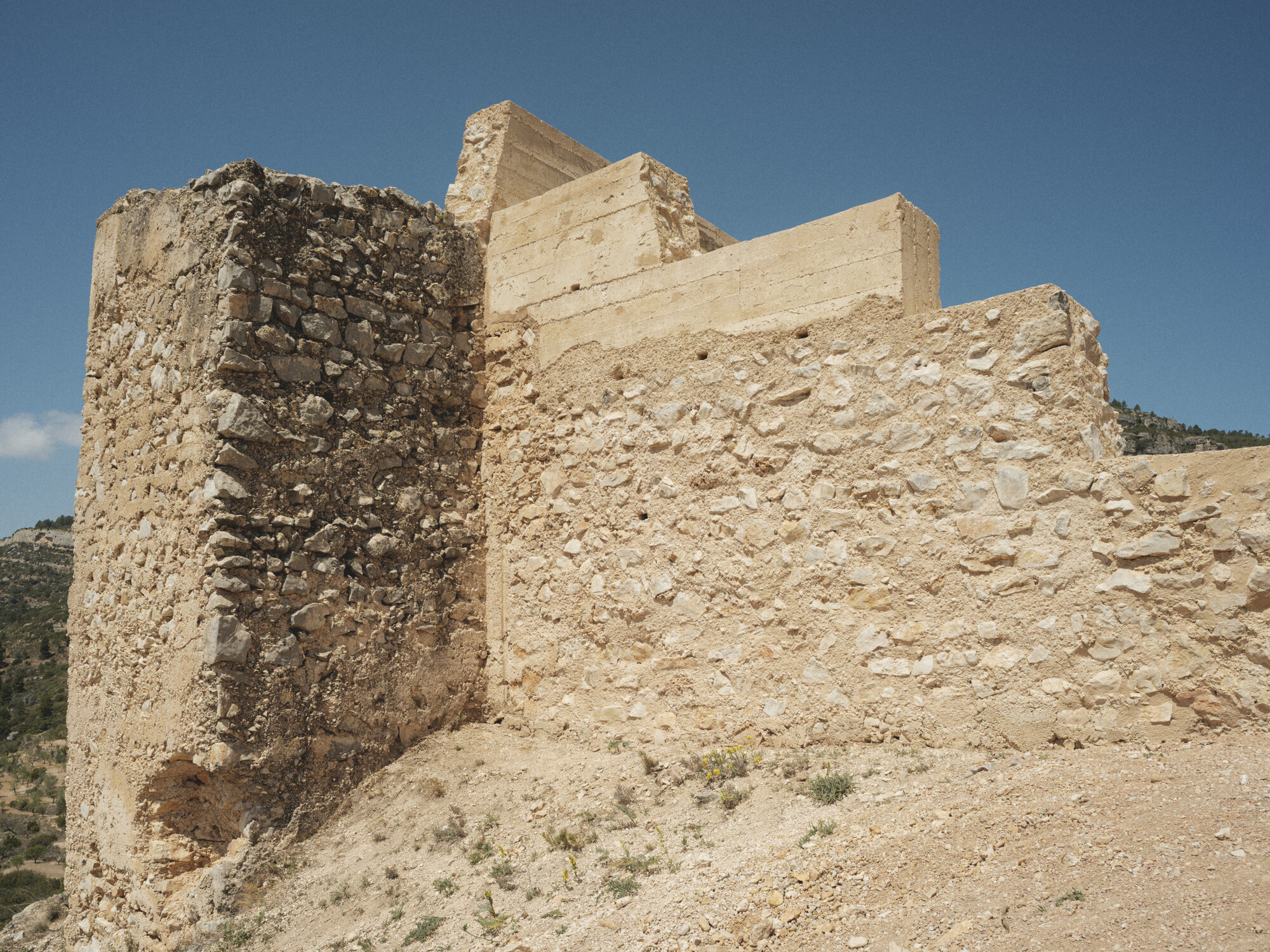 Weathered stone fortification walls with cylindrical tower rising against a clear blue sky