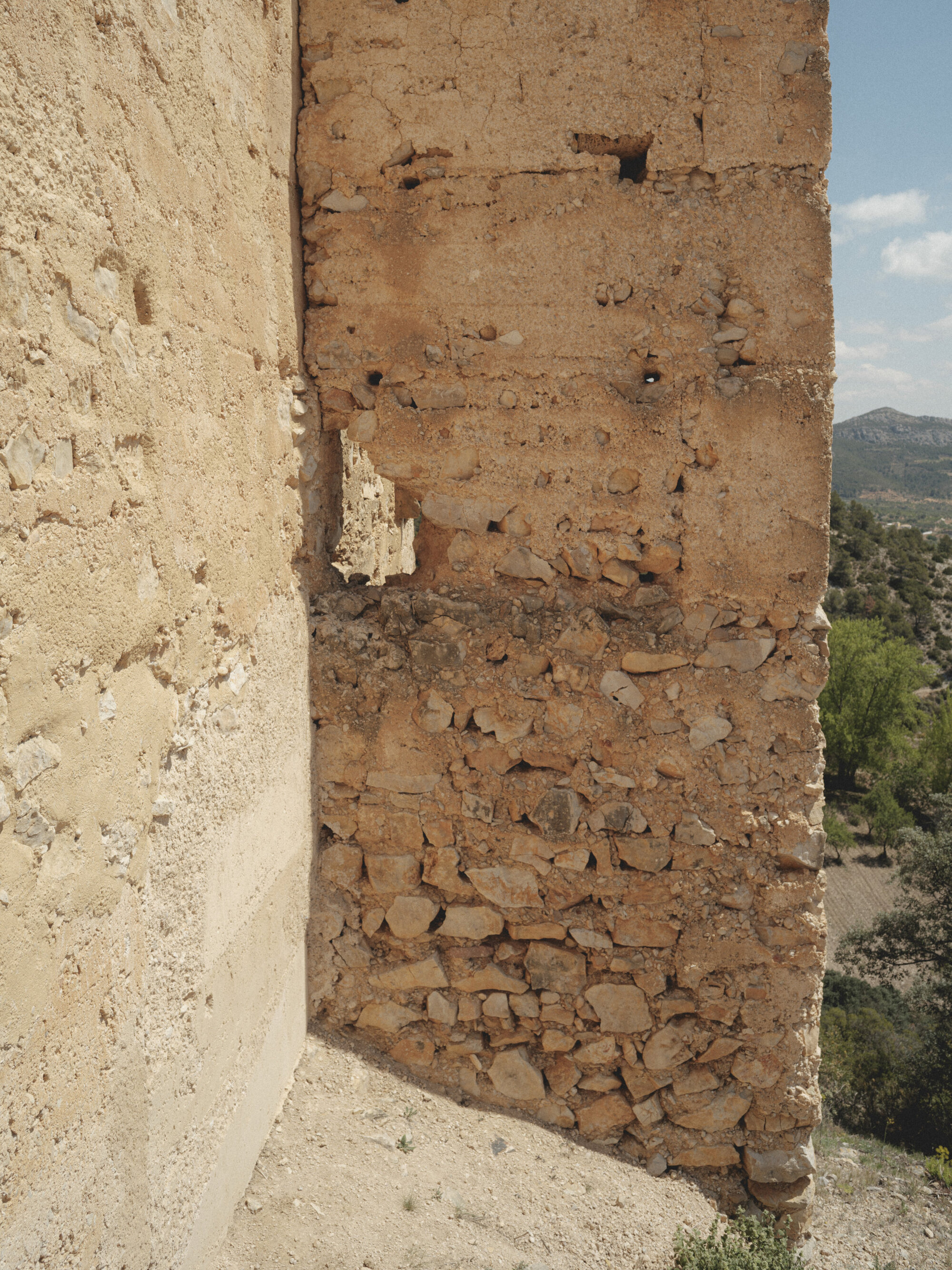 Close-up of layered rammed earth wall section showing horizontal construction lines and erosion