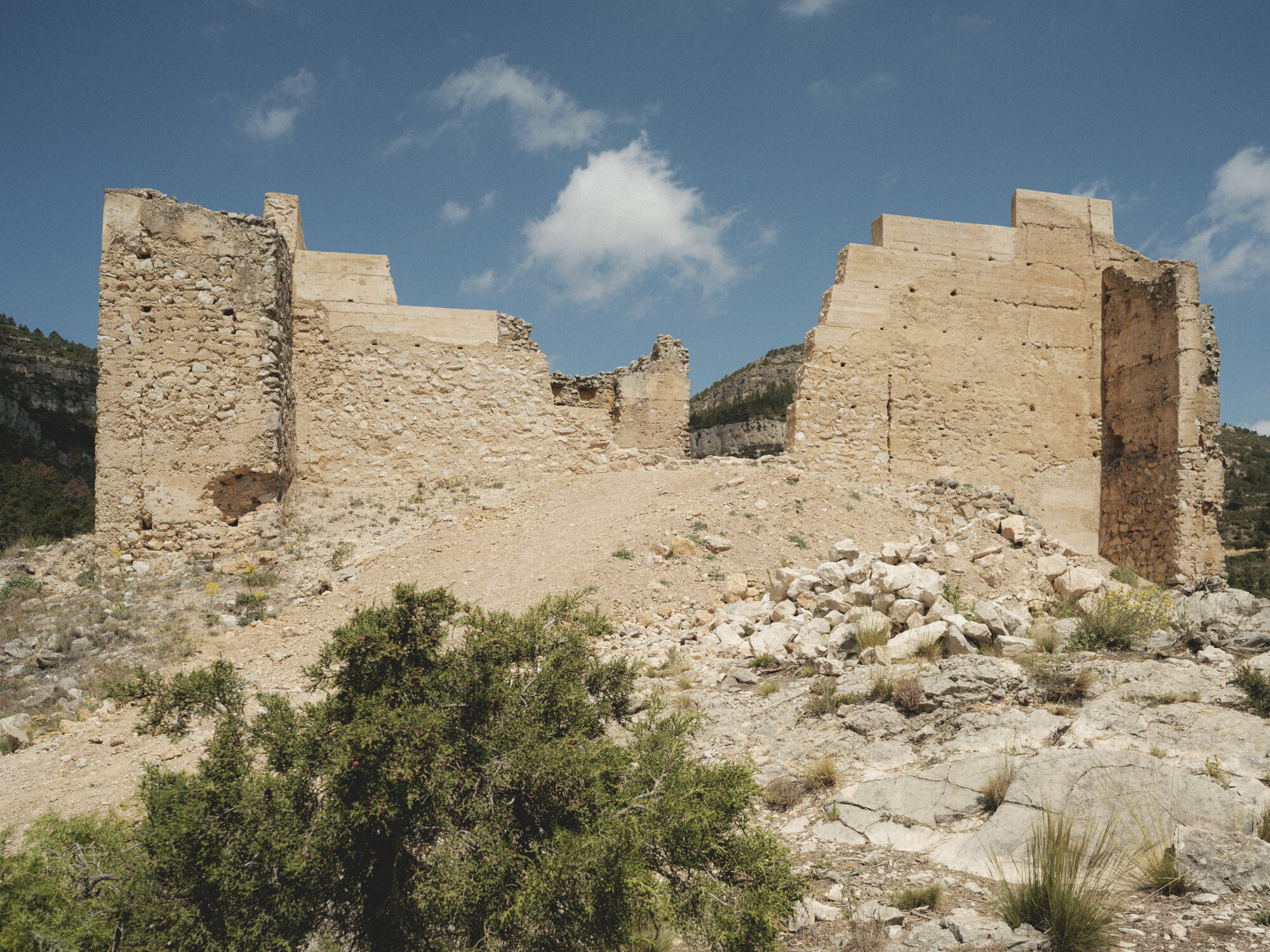 Ruins of fortification walls and towers on limestone outcrop with sparse vegetation