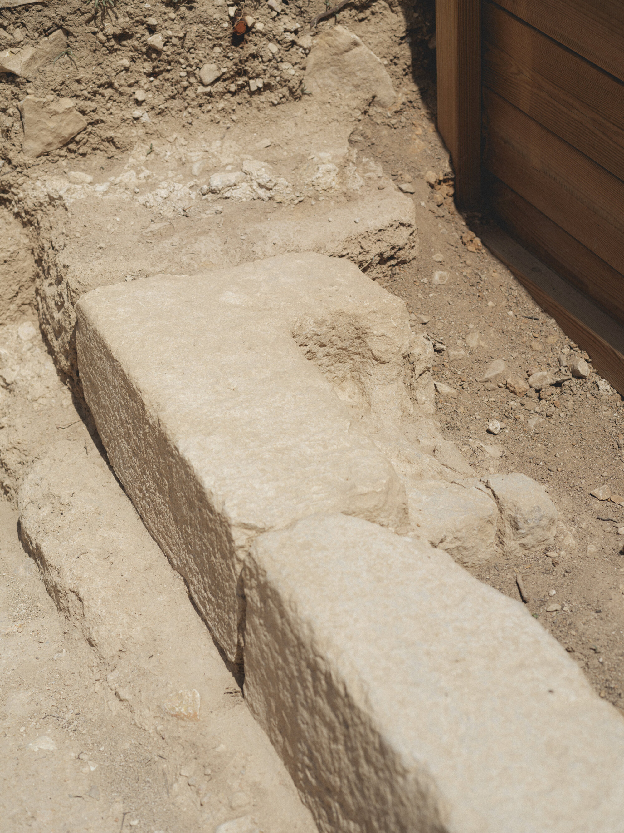 Cut stone blocks forming steps in excavated earth beside timber wall edge