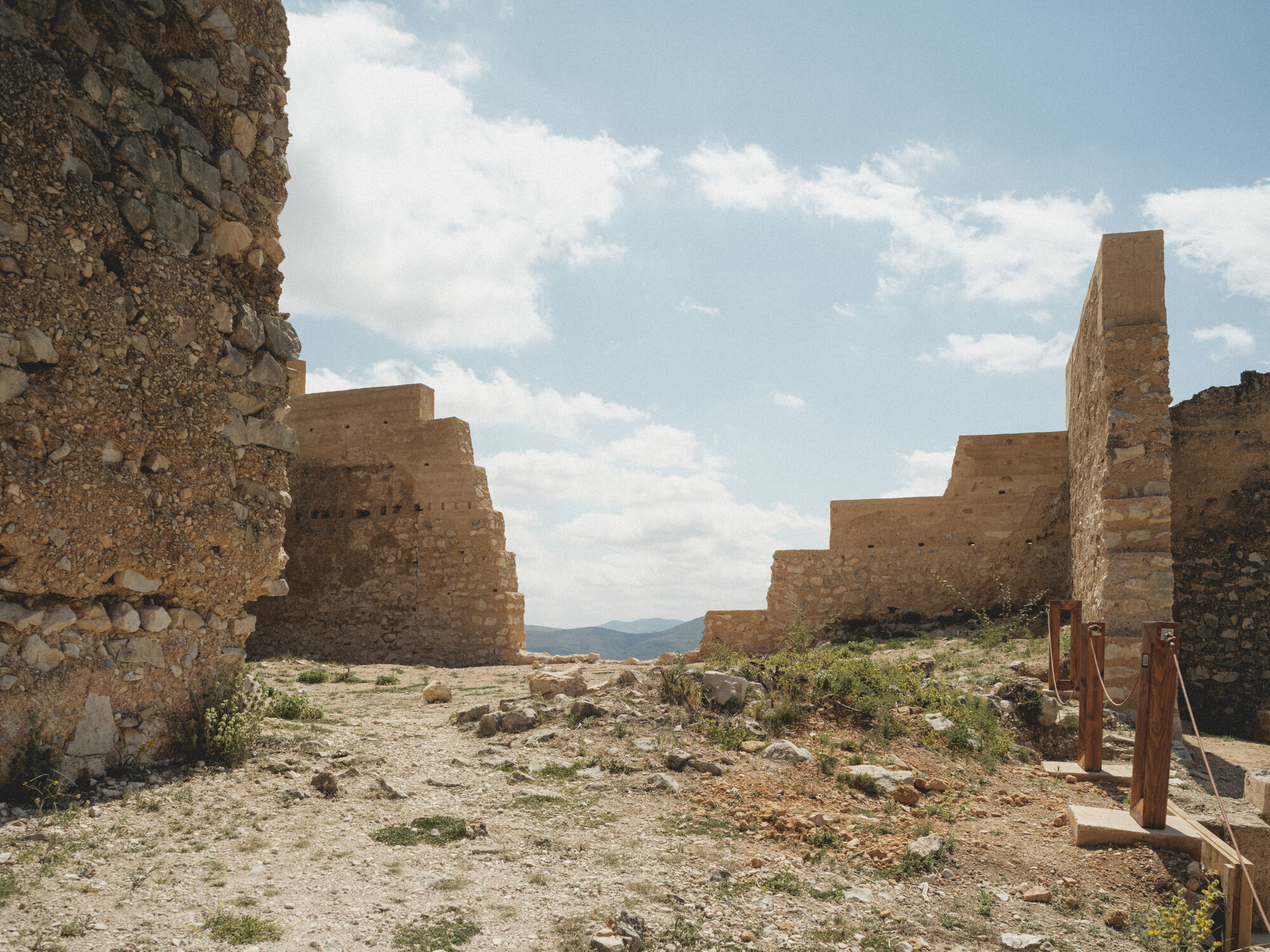 Courtyard space framed by deteriorating masonry walls with distant mountain ranges visible