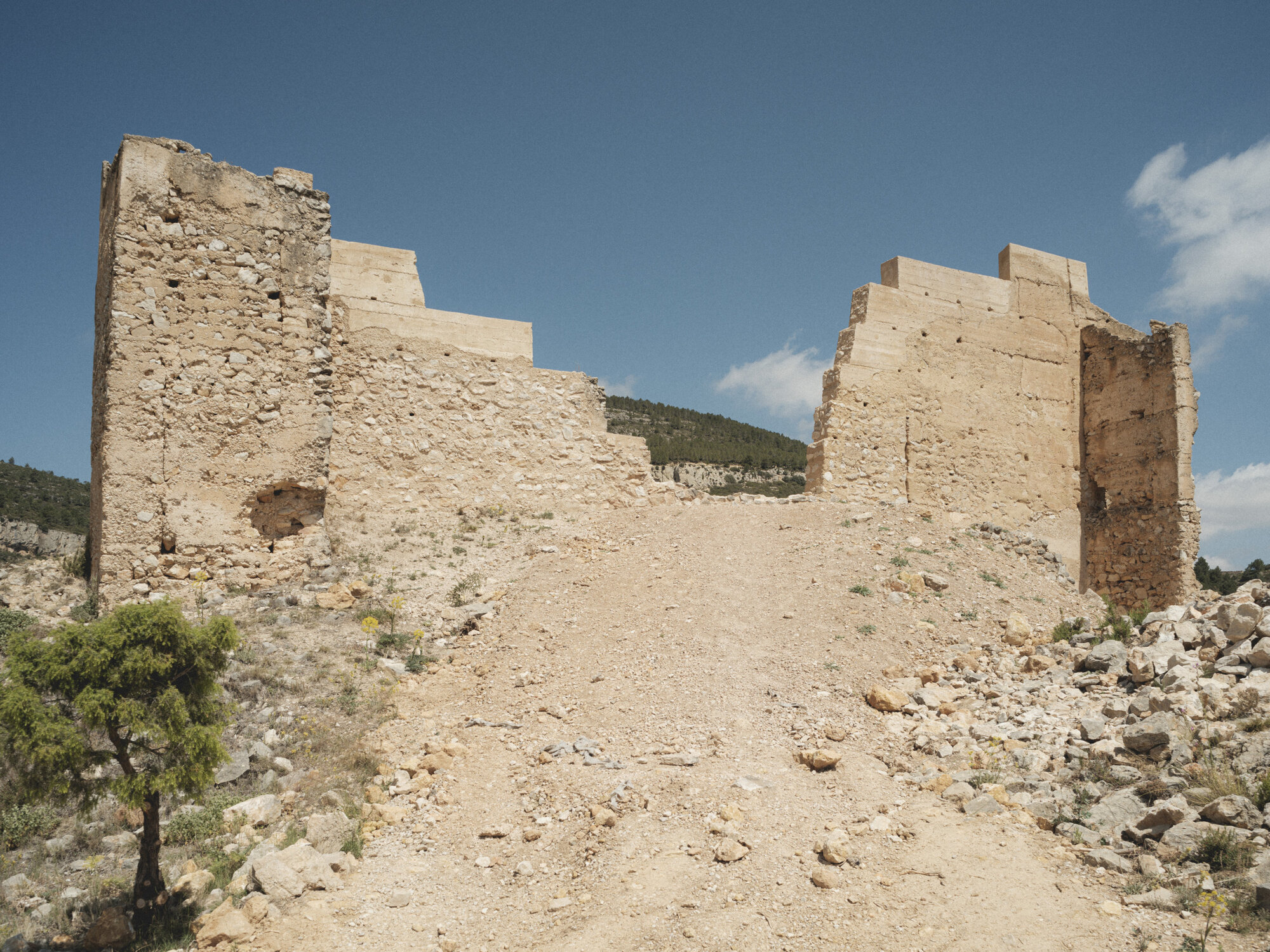 Stepped rammed earth walls flanking a gravel path ascending a hillside under clear blue sky