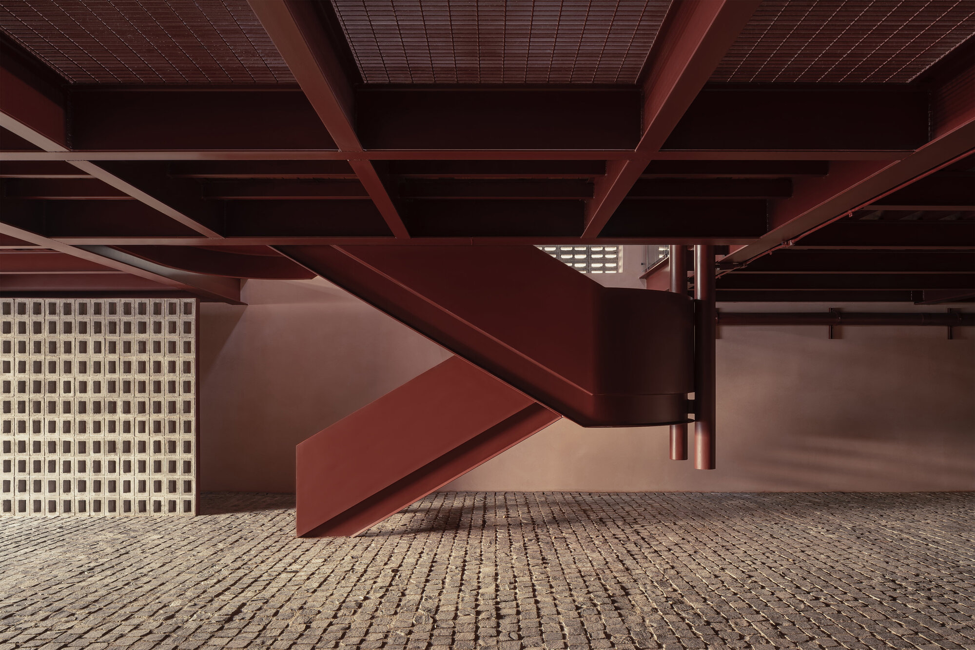 Covered ground-level parking area with exposed steel beams and perforated block screen wall