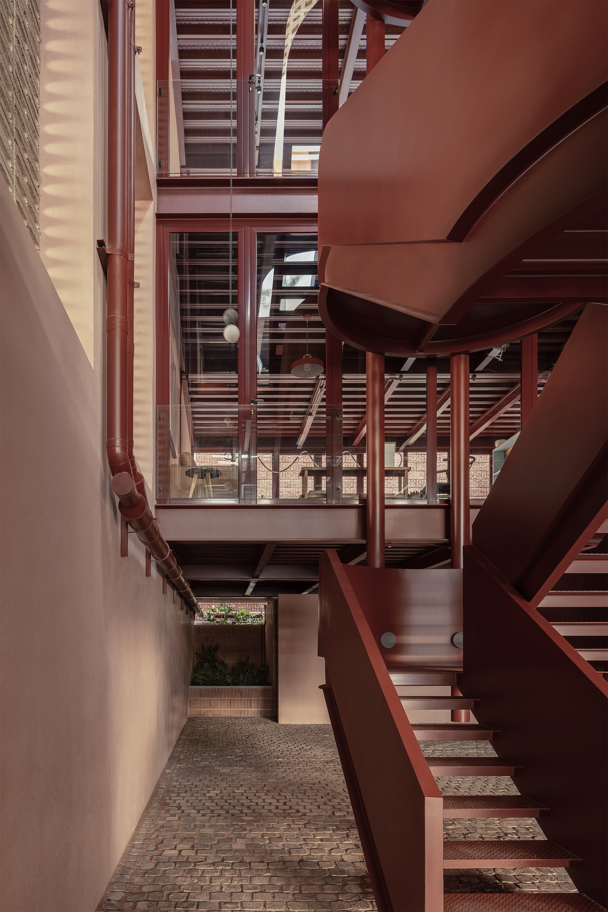 Narrow courtyard passage with red steel stairs and bridges connecting levels beneath slatted screens