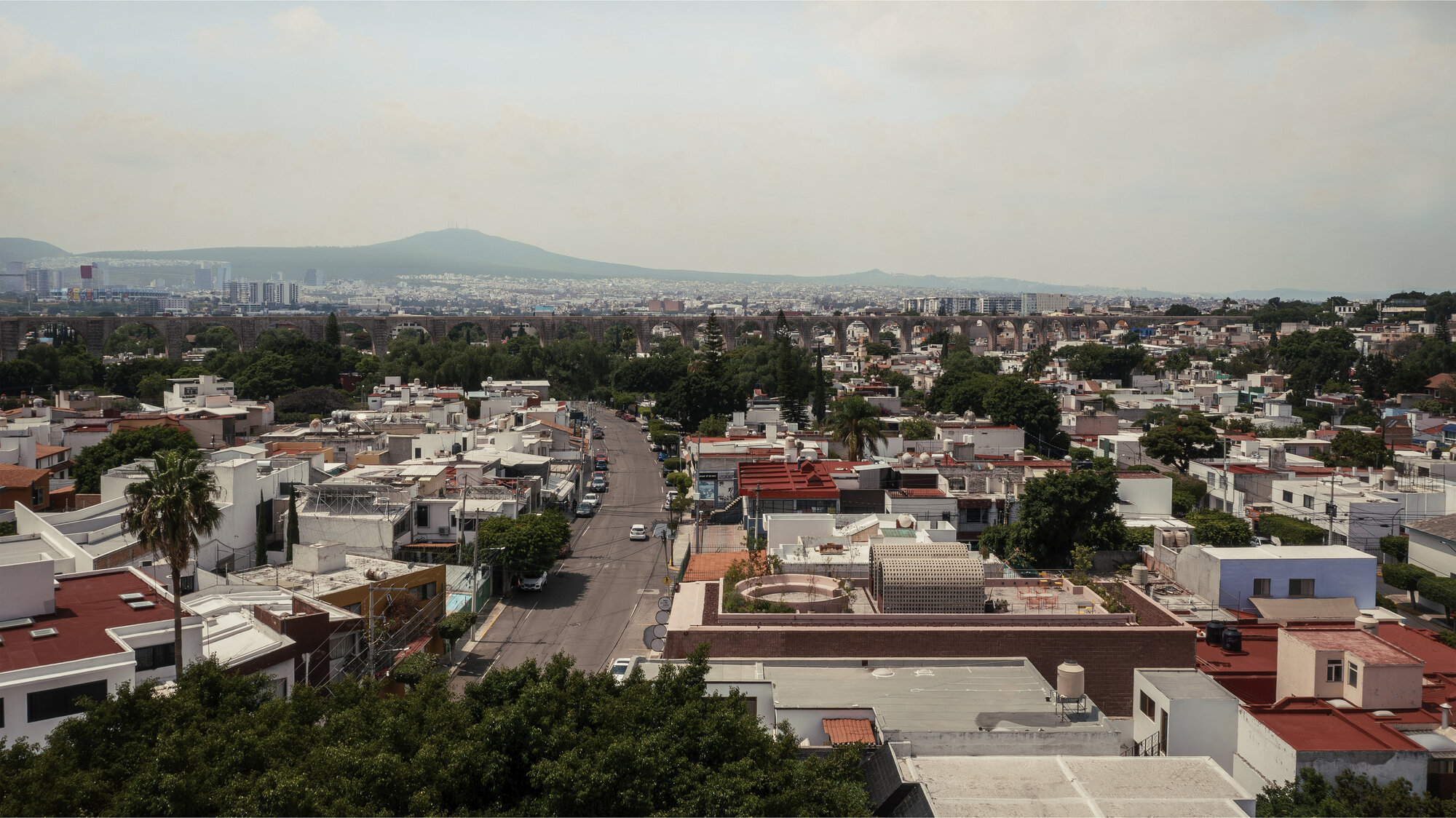 Wide aerial view of low-rise residential rooftops with mountains visible on the horizon under hazy afternoon light
