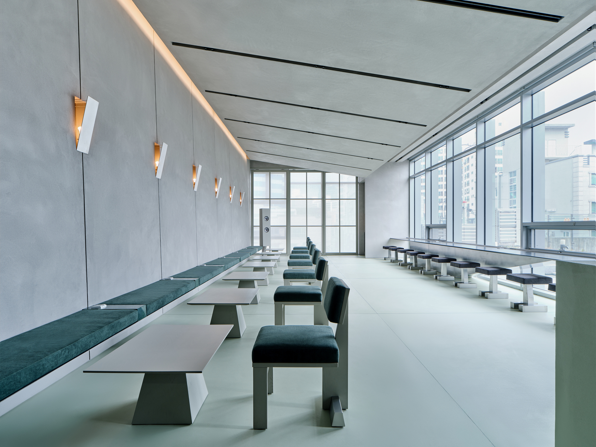 Long room with white tables flanked by teal seating under a coved ceiling with linear recessed lighting