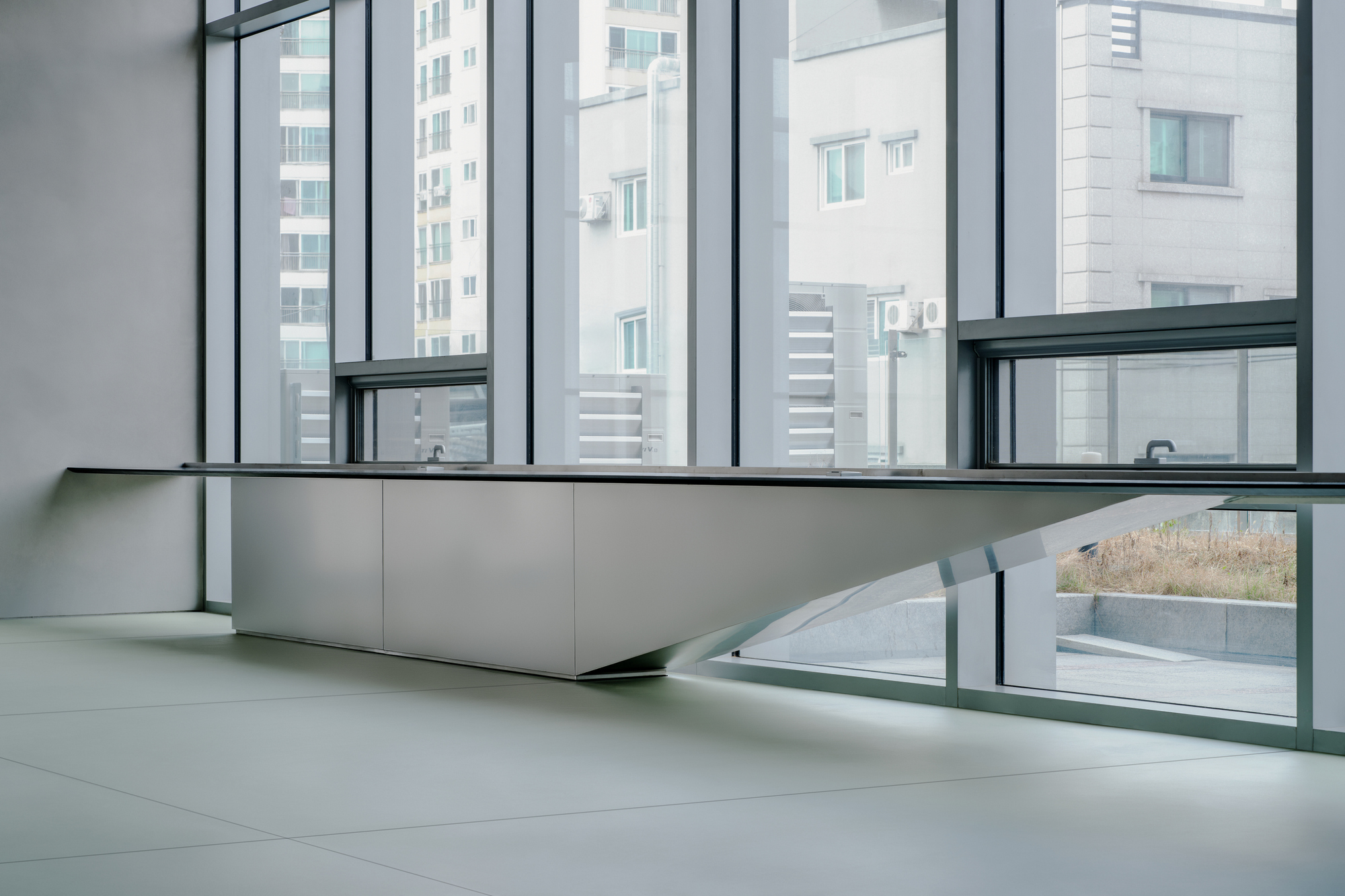 Low angled view of a continuous bench below full-height glazing overlooking adjacent tower blocks