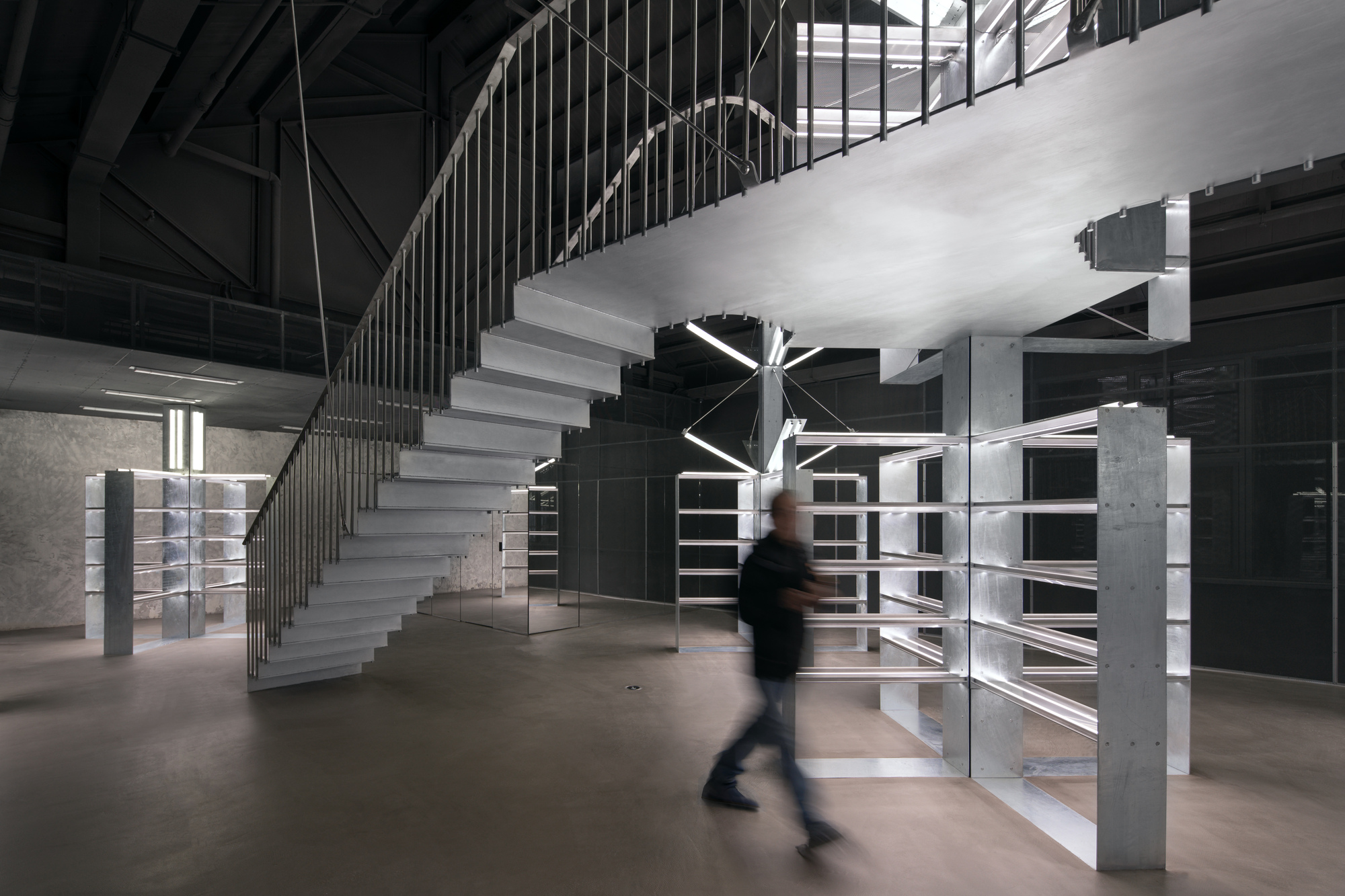 Concrete staircase with vertical metal balustrade and a figure crossing the polished floor below
