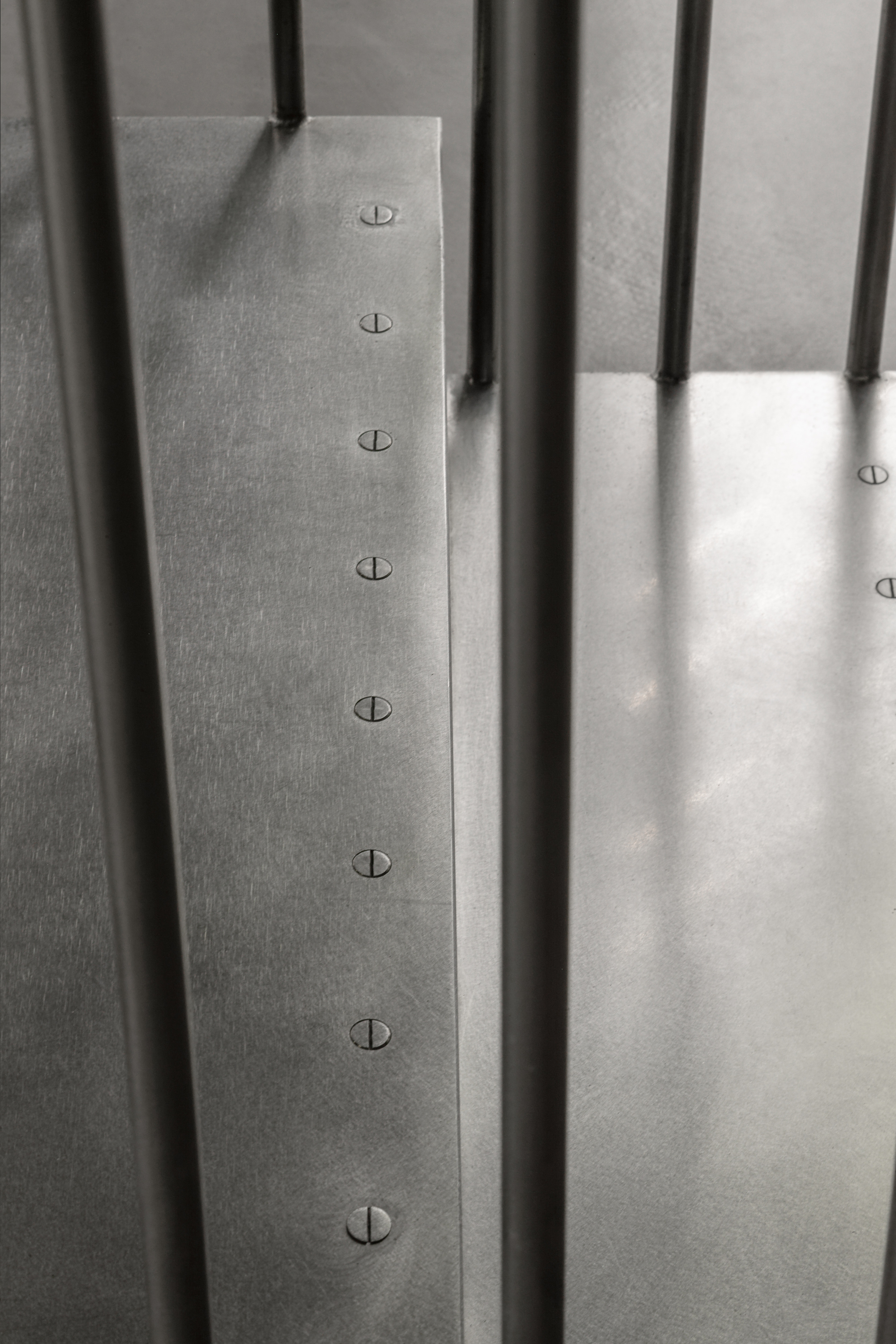 Detail of vertical steel rods penetrating a brushed metal plate with countersunk fasteners