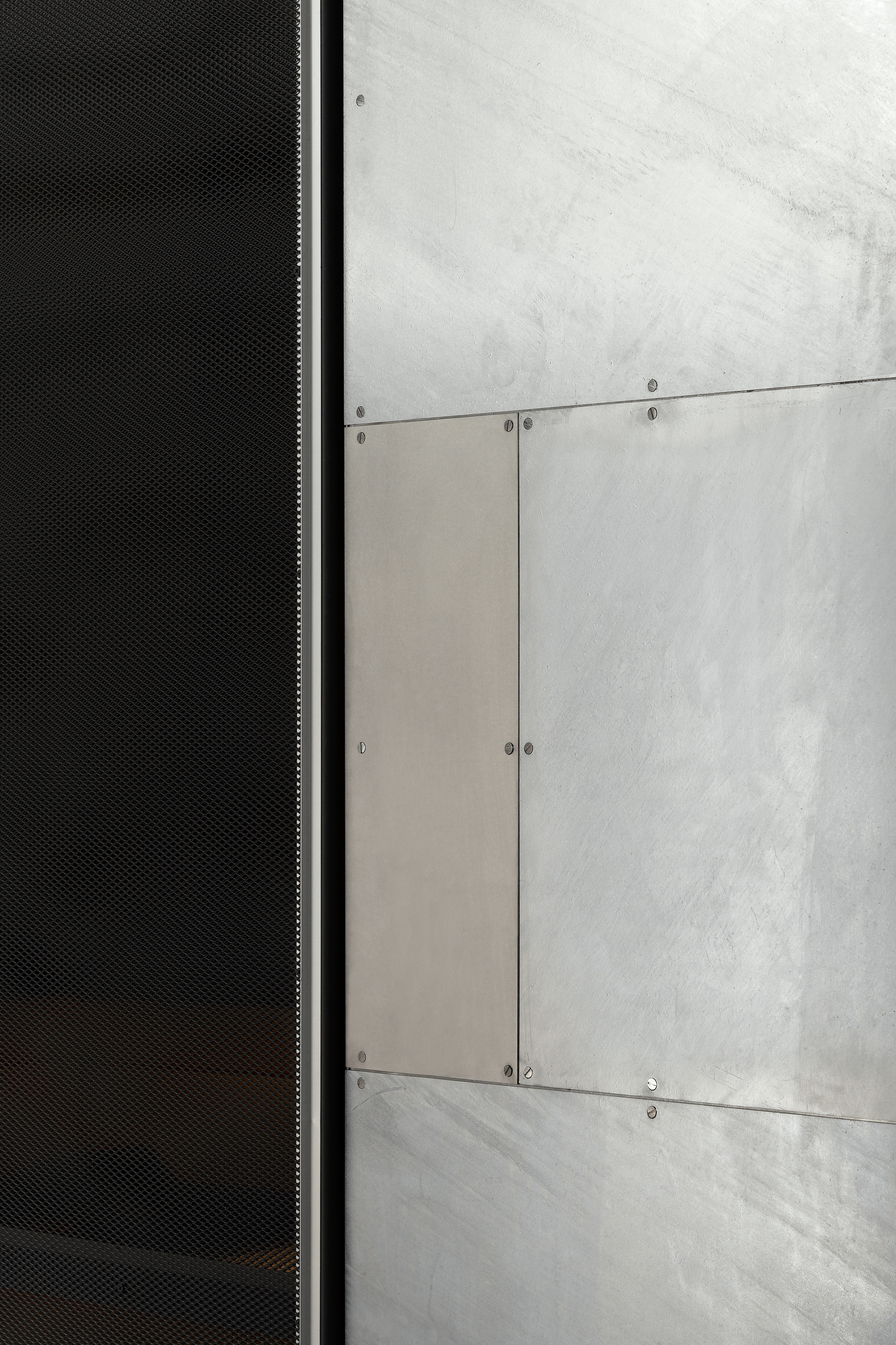 Junction between black perforated metal panel and raw concrete wall with exposed screws
