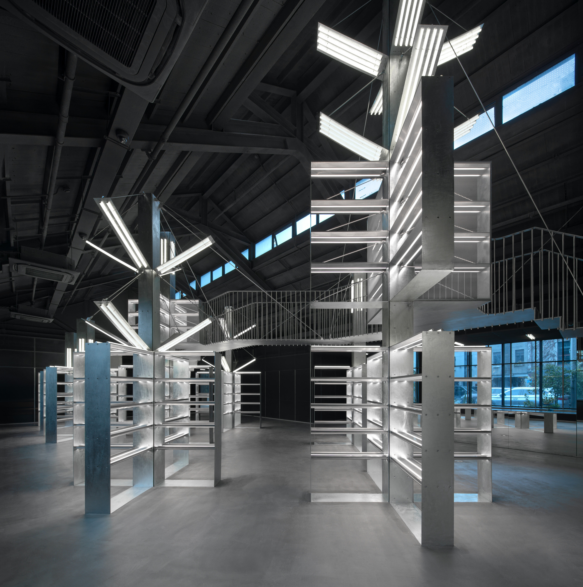 Library shelving with fluorescent tube lighting arranged in geometric clusters under industrial ceiling