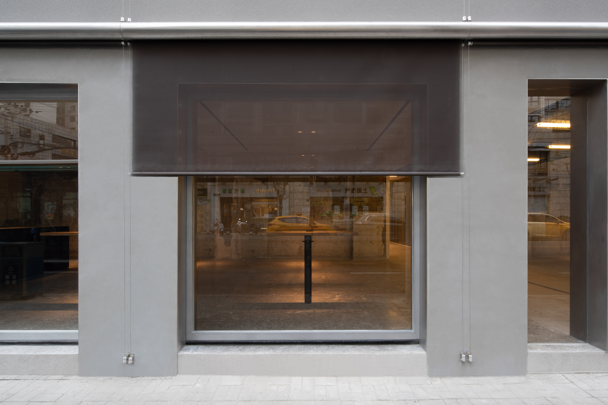 Street facade with gray metal panels and retractable mesh screens above the glazed storefront opening
