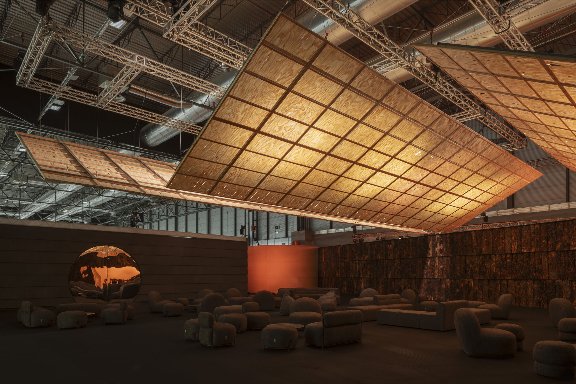 Curved plywood ceiling suspended over a lounge area with rounded seating and exposed truss infrastructure