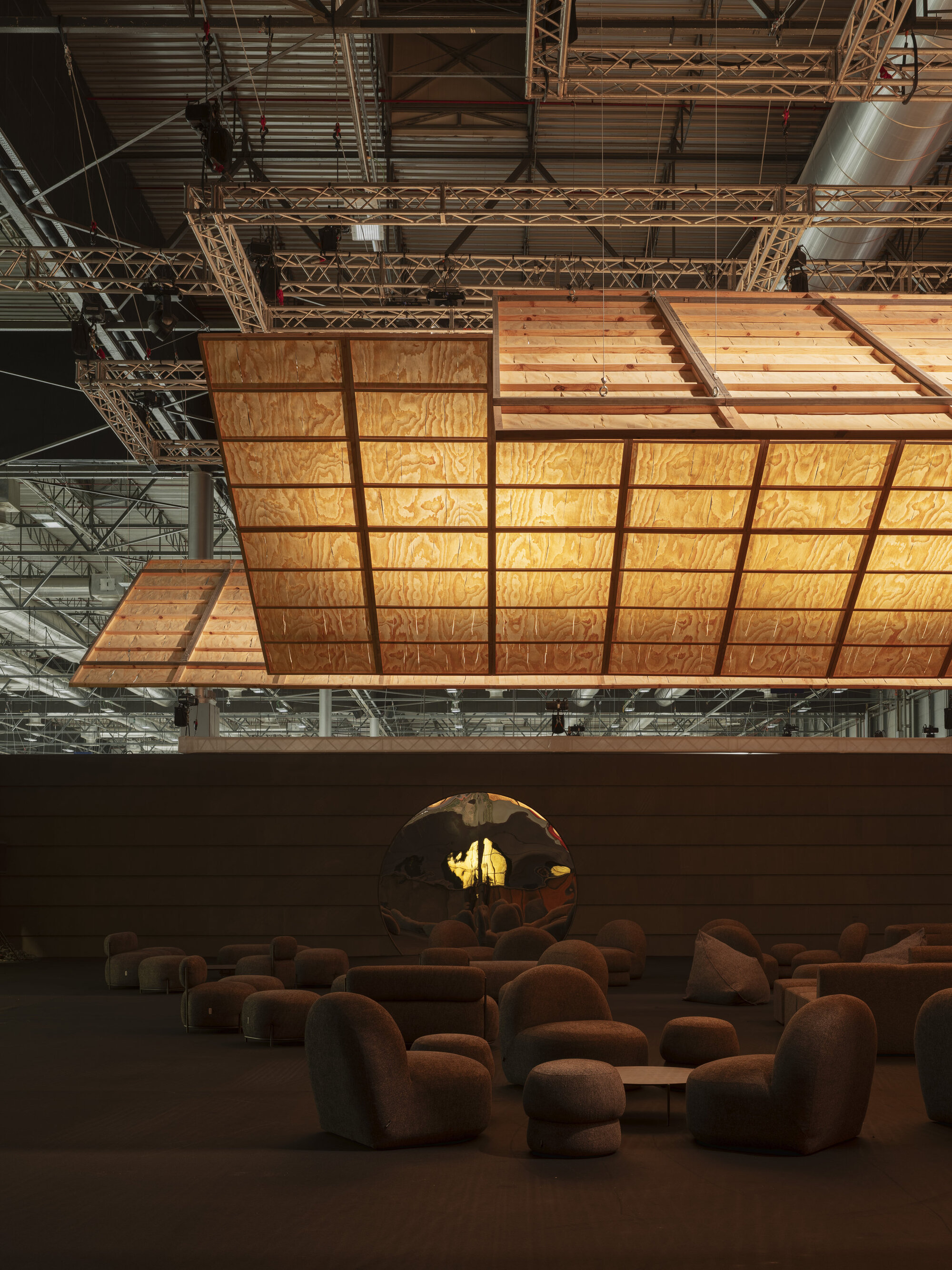Angled view of the suspended plywood ceiling panels with metal truss rigging and sculptural seating below