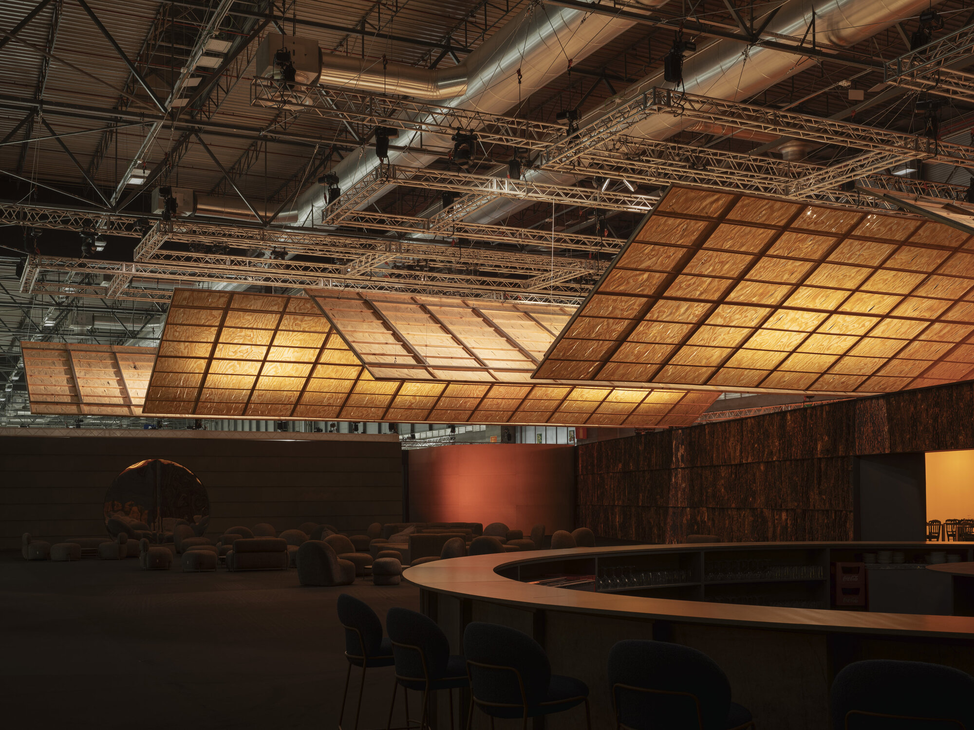 Undulating backlit timber grid ceiling suspended over a gallery space with curved seating and bark-clad walls