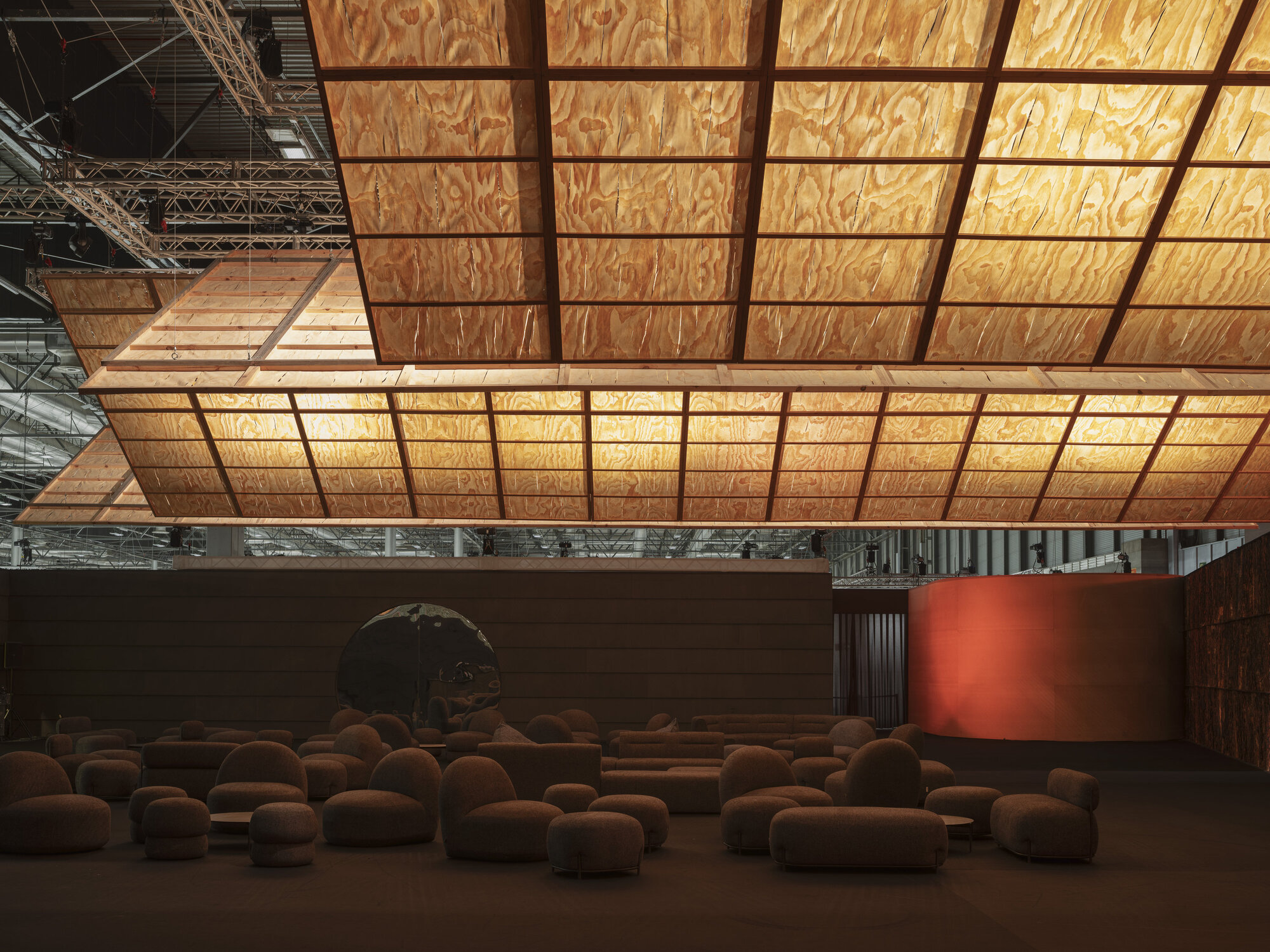 Interior view of the gridded plywood ceiling plane with metal frame above scattered upholstered seating below