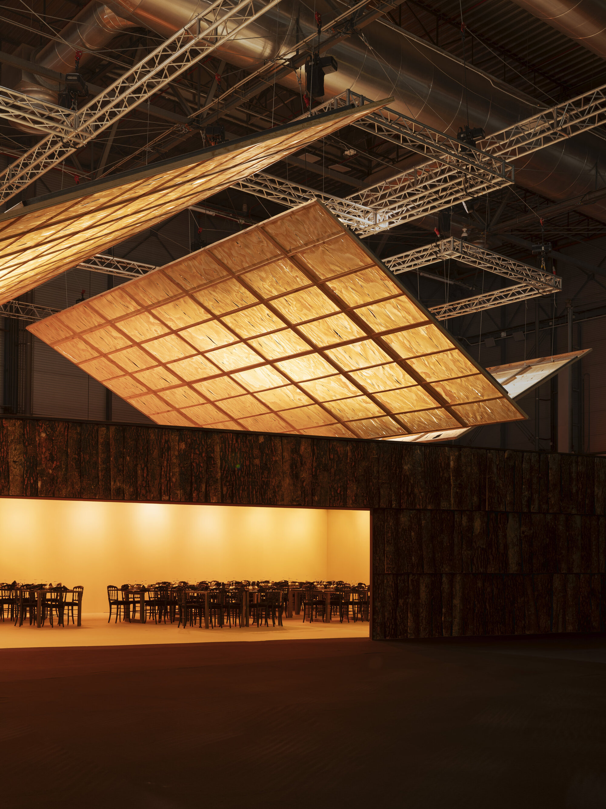 Suspended gridded ceiling panel with timber framing and translucent infill above a dark timber-clad wall
