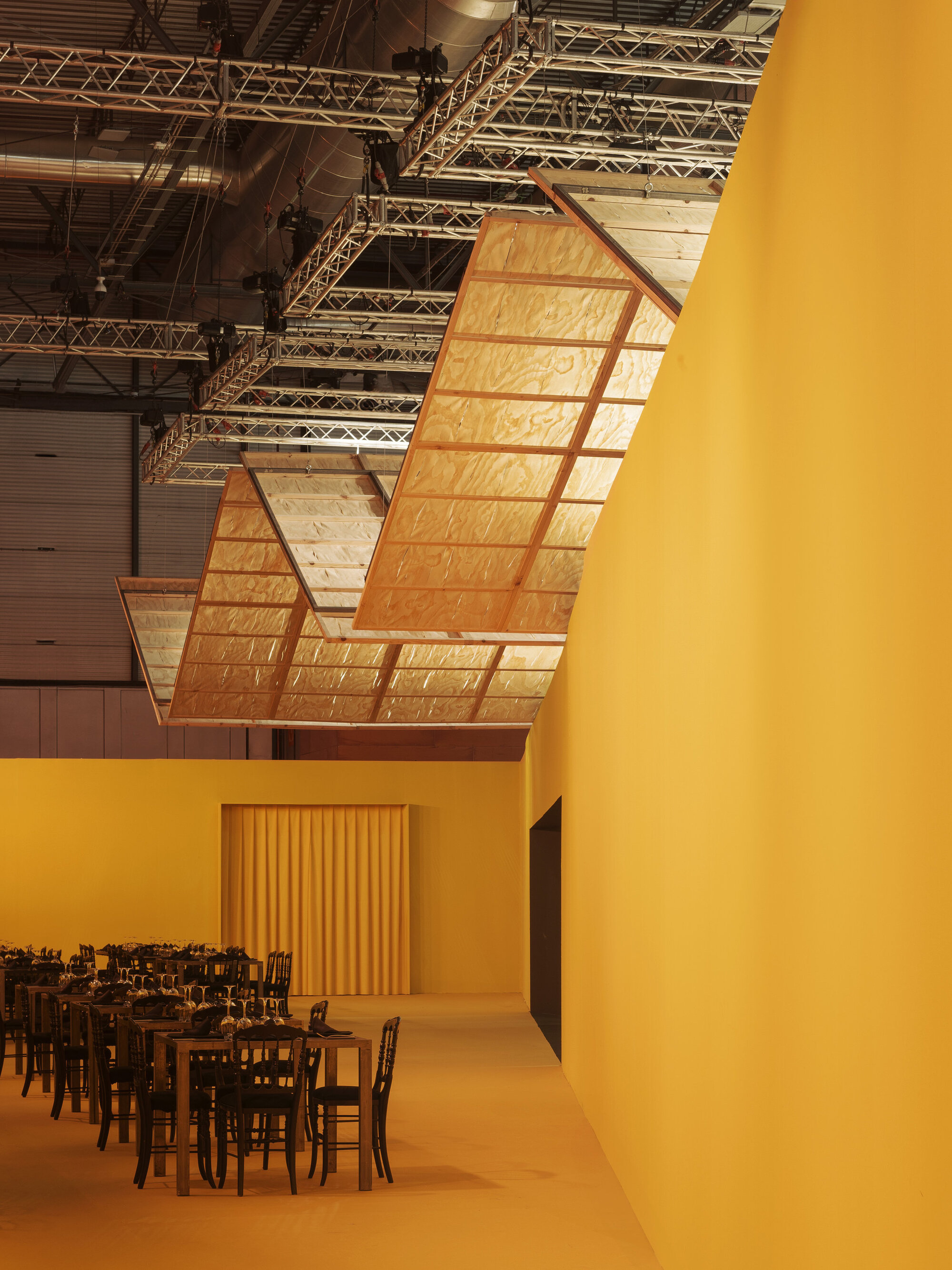 Curved suspended ceiling panel beside a yellow-painted wall and doorway with vertical timber slats
