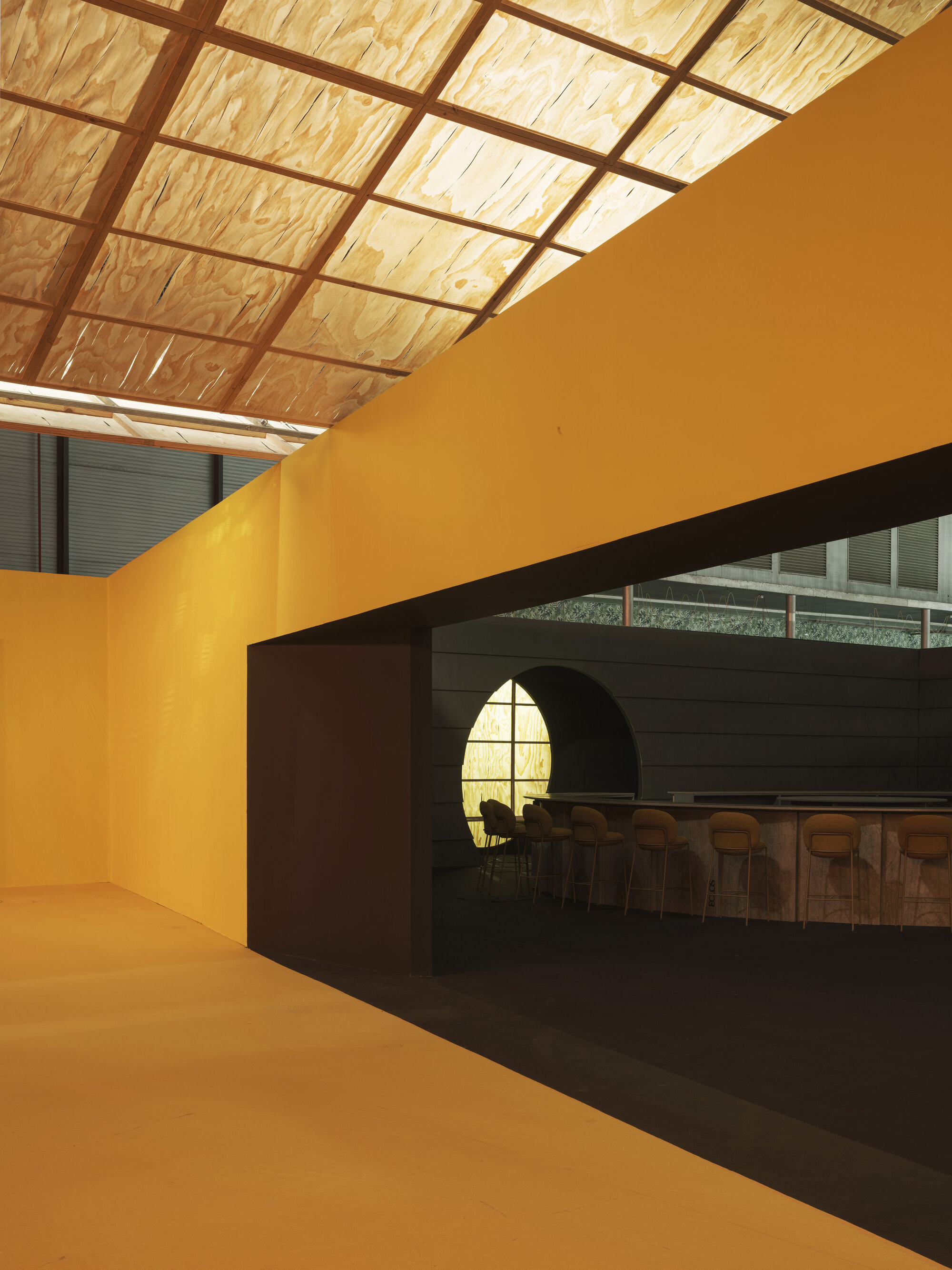Yellow painted wall with arched opening framing a view to a bar area beneath gridded ceiling
