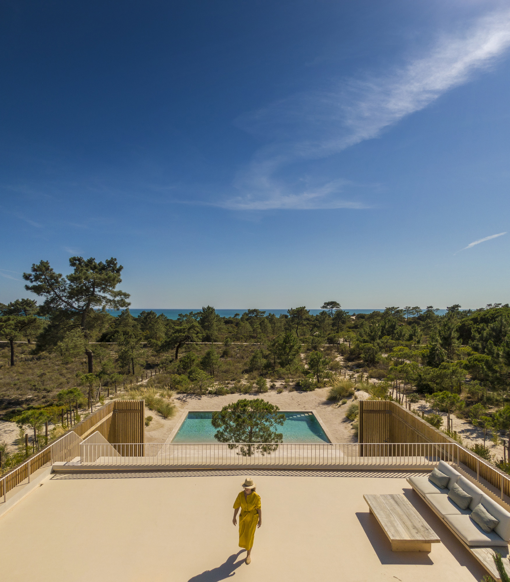 Rooftop terrace overlooking pool and pine forest with a person walking below