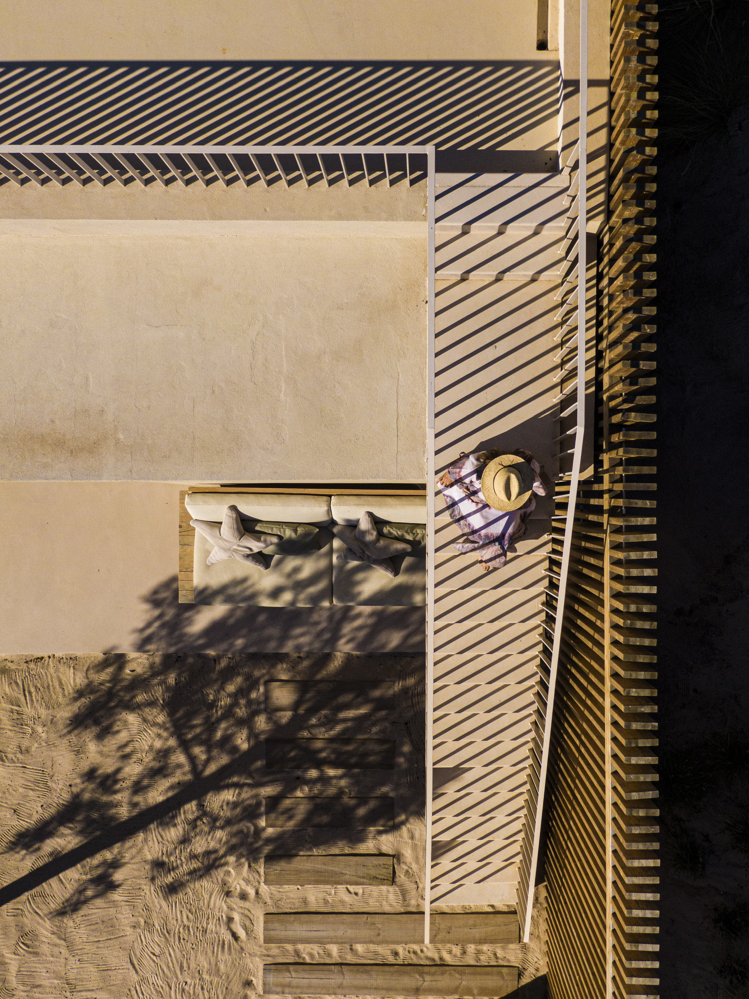 Aerial view of terrace with slatted timber screen casting shadows on pale stone paving and figure seated below