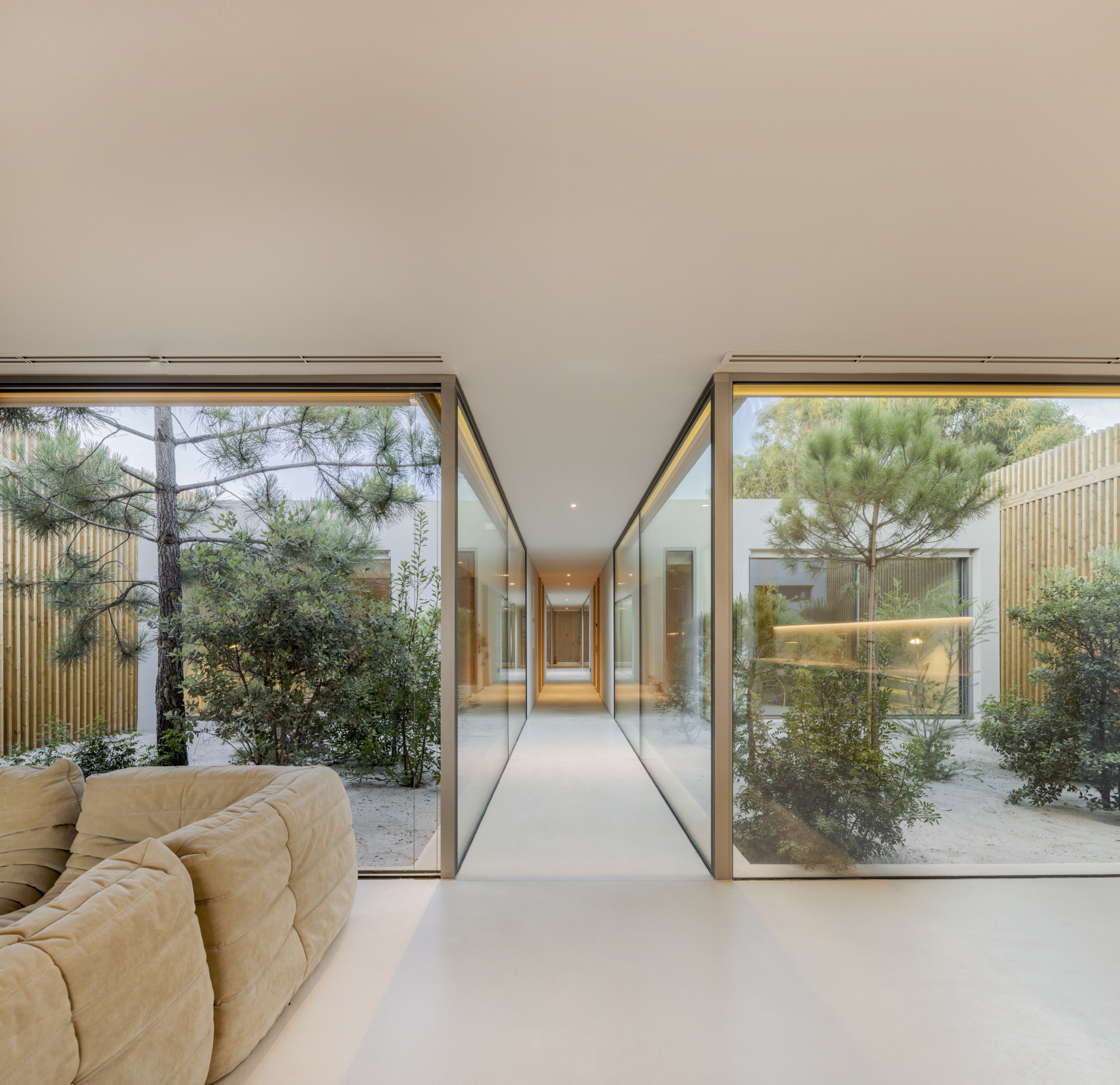 Living space with floor-to-ceiling glass walls opening to planted courtyards on both sides