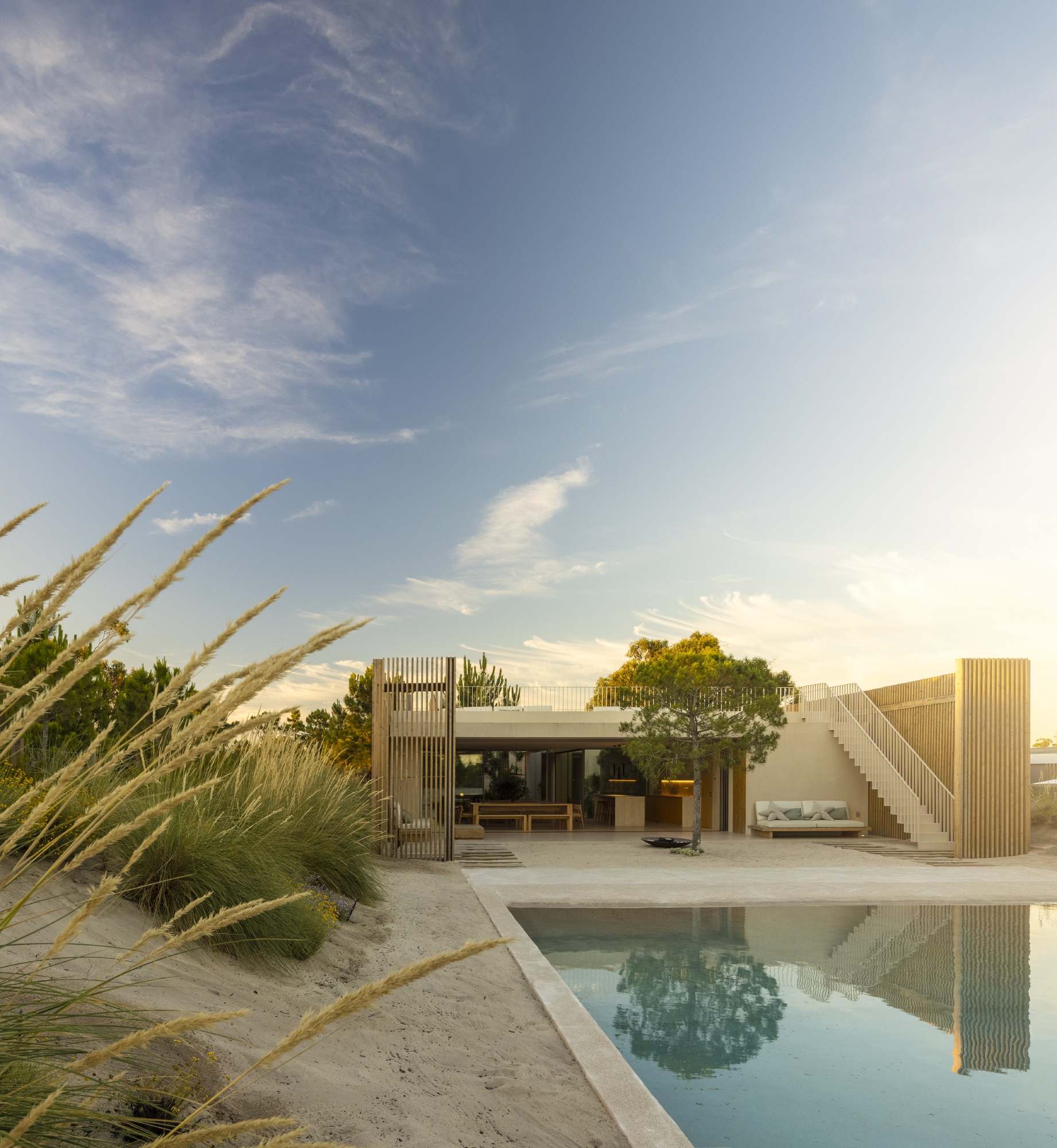 Pool terrace facing timber-clad volumes with outdoor stairs and ornamental grasses at dusk