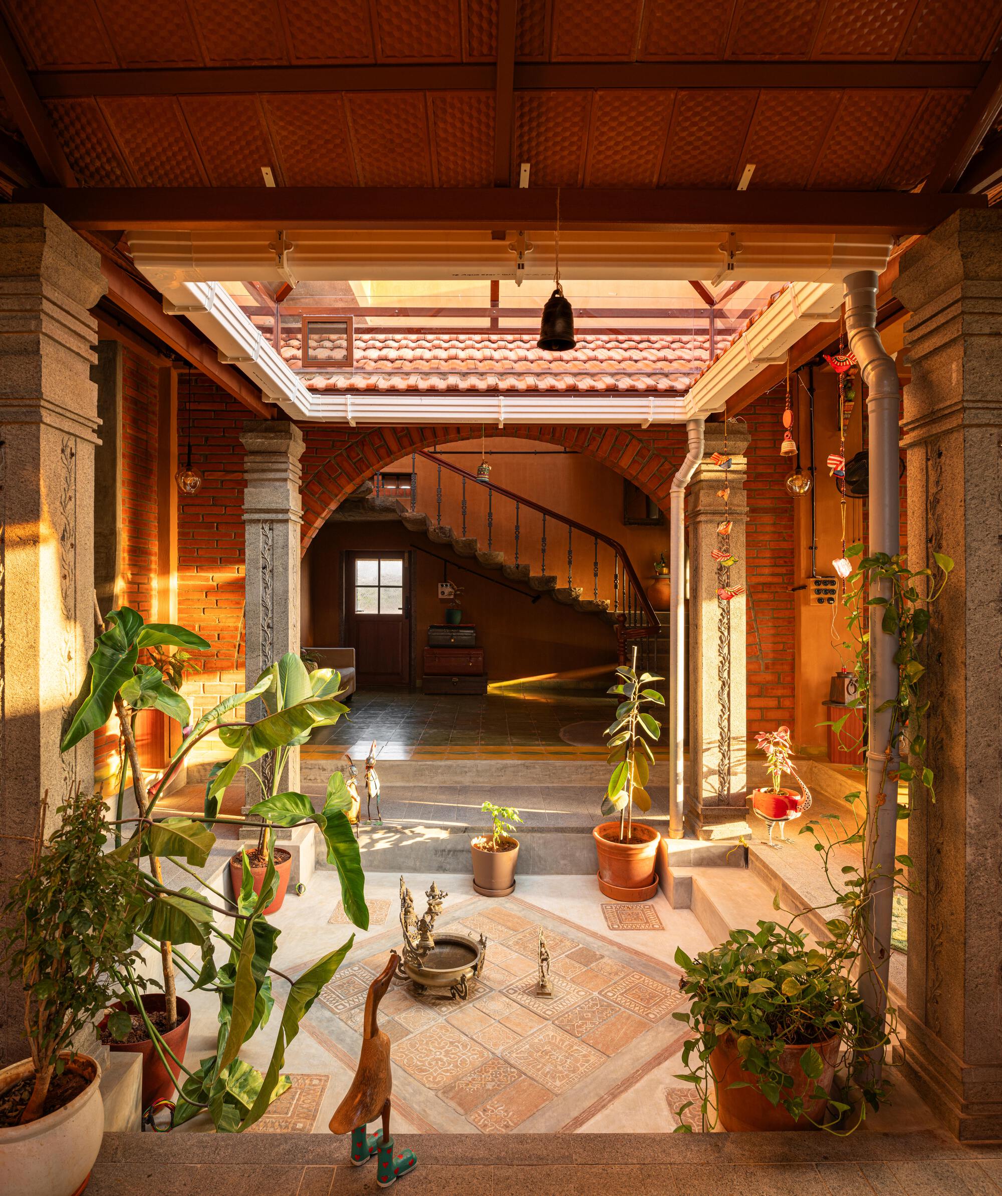 Interior courtyard with potted plants, carved stone columns, curved staircase and woven bamboo ceiling