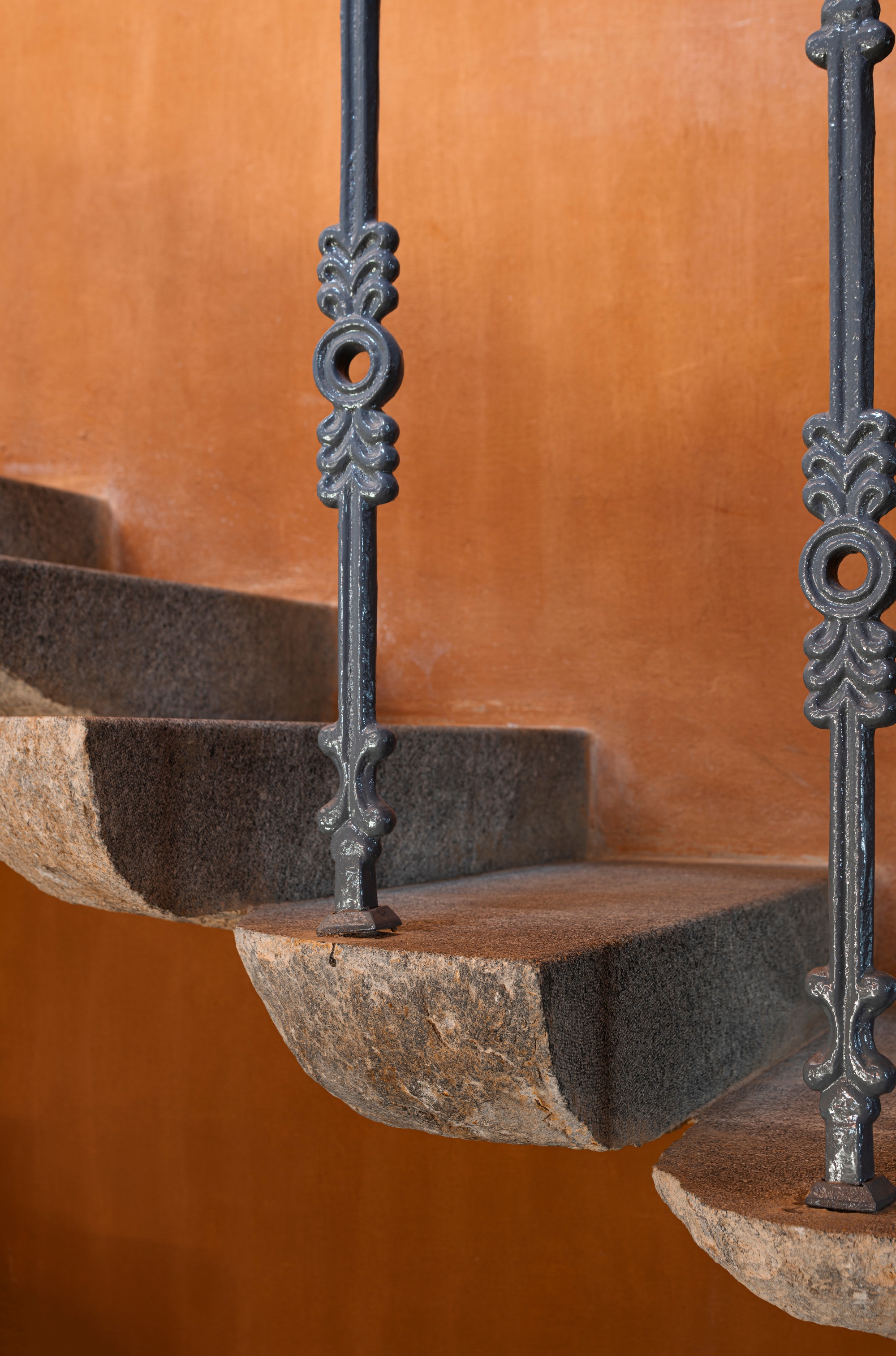 Detail of ornate wrought iron balusters with stone treads against an orange plaster wall