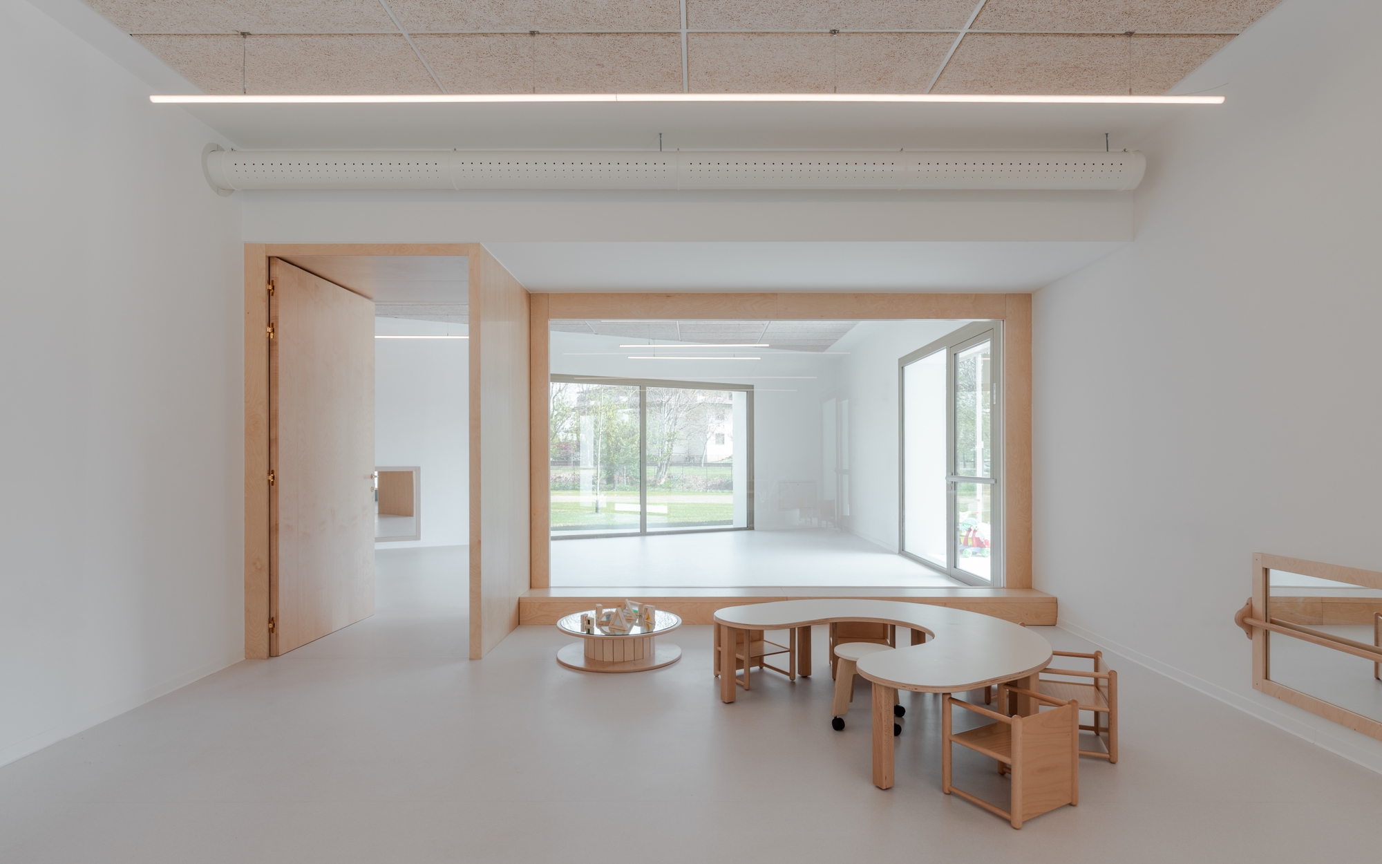 Interior space with timber window seat overlooking the lawn and curved wooden tables on resin flooring
