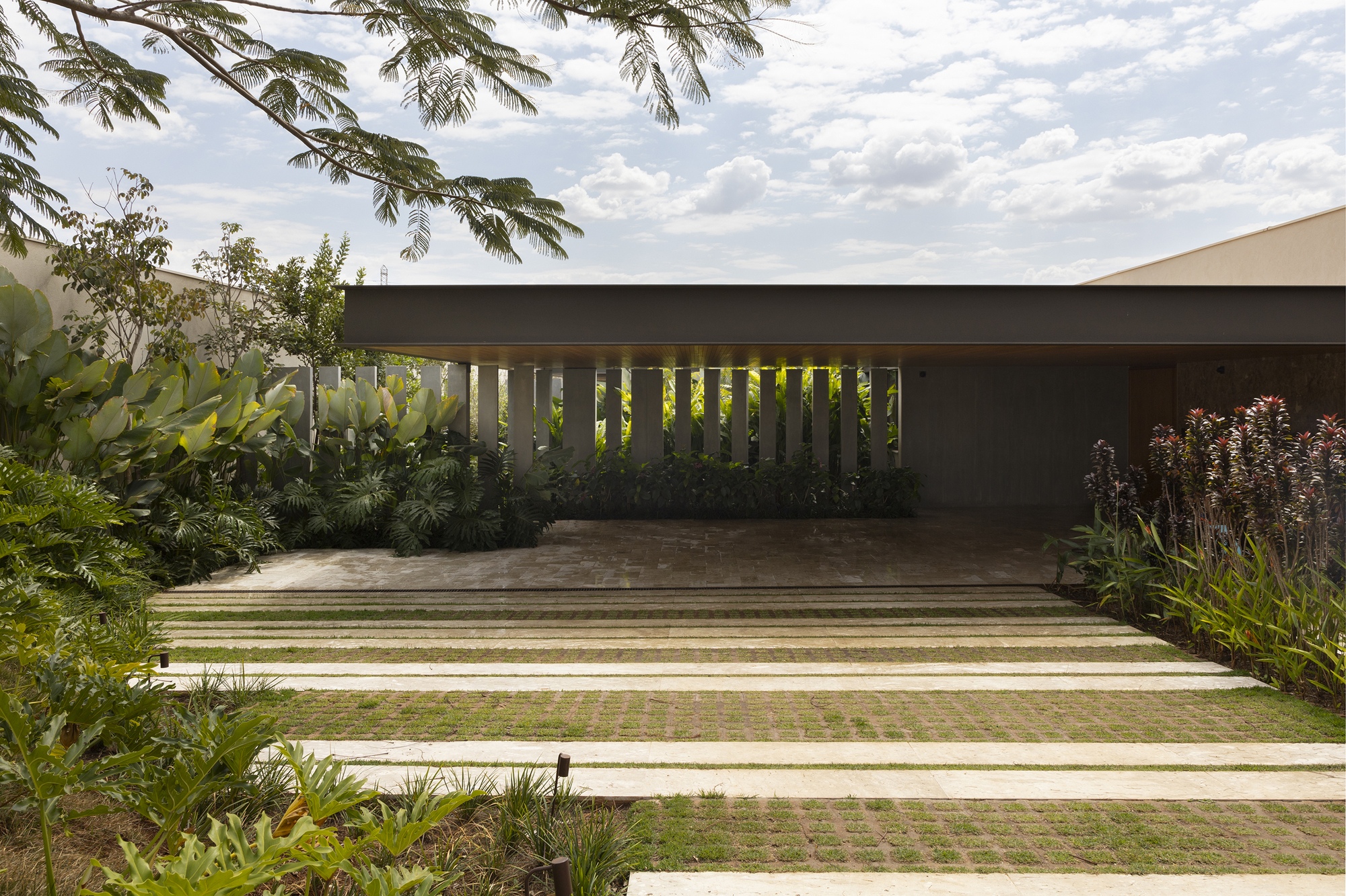 Concrete drive with alternating grass strips leading to a covered carport with vertical metal screens
