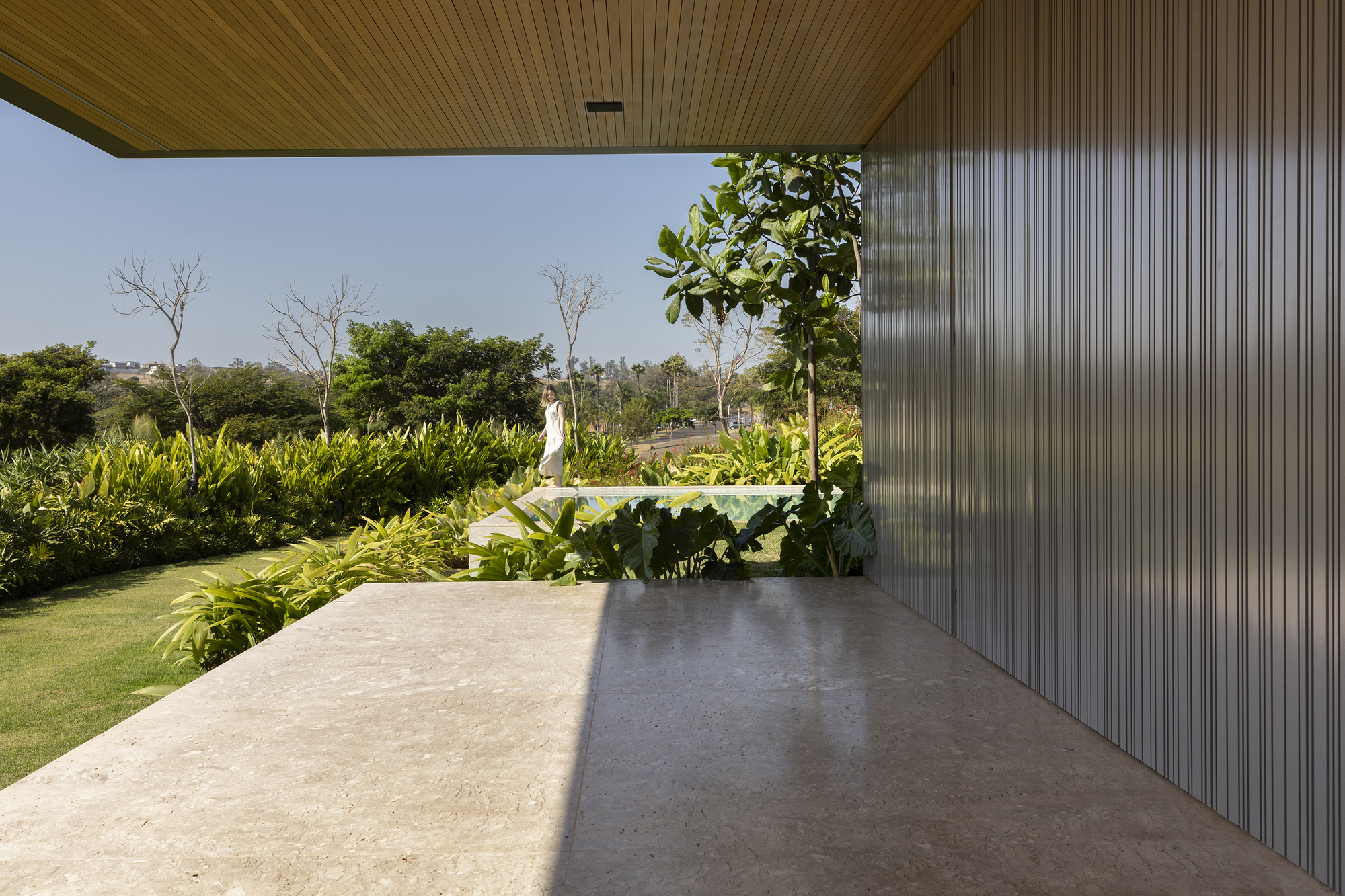 Covered terrace with slatted timber ceiling and corrugated metal wall overlooking planted garden
