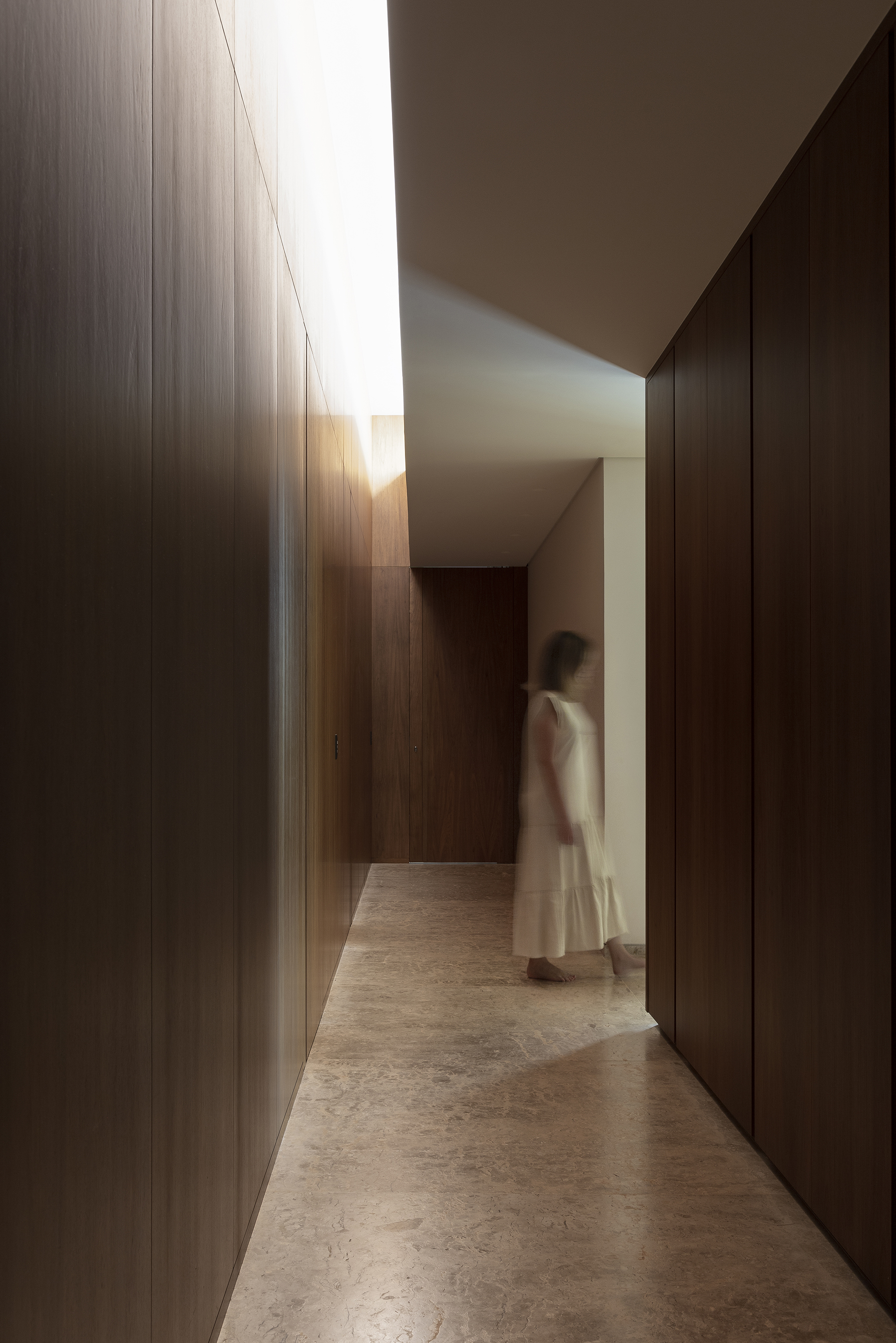 Corridor with floor-to-ceiling timber wall panels and natural light filtering through a clerestory above