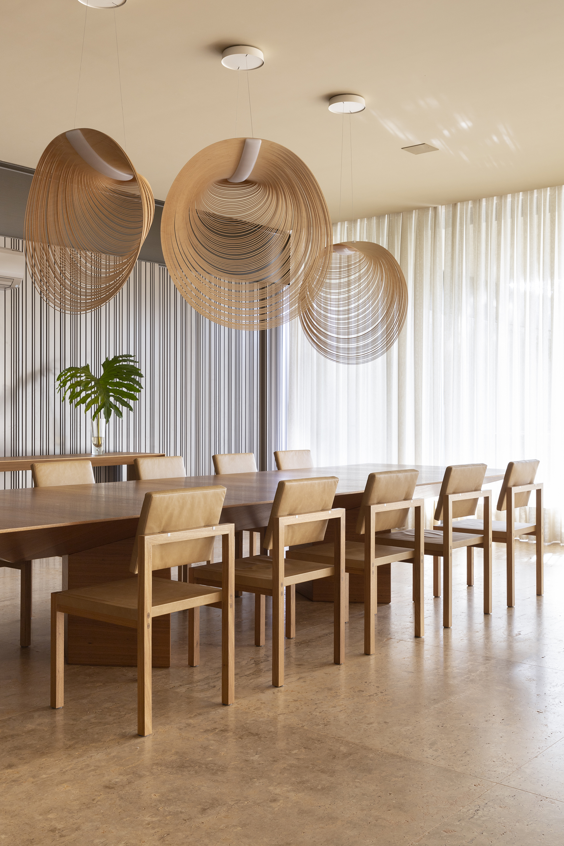 Dining room with layered circular timber pendant lights suspended over a long table and chairs