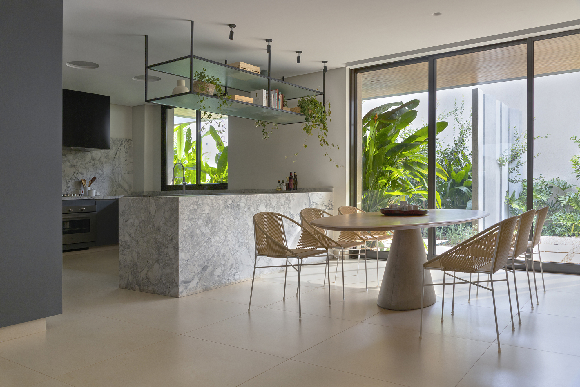 Open kitchen and dining area with marble island and glazed walls framing tropical plantings outside