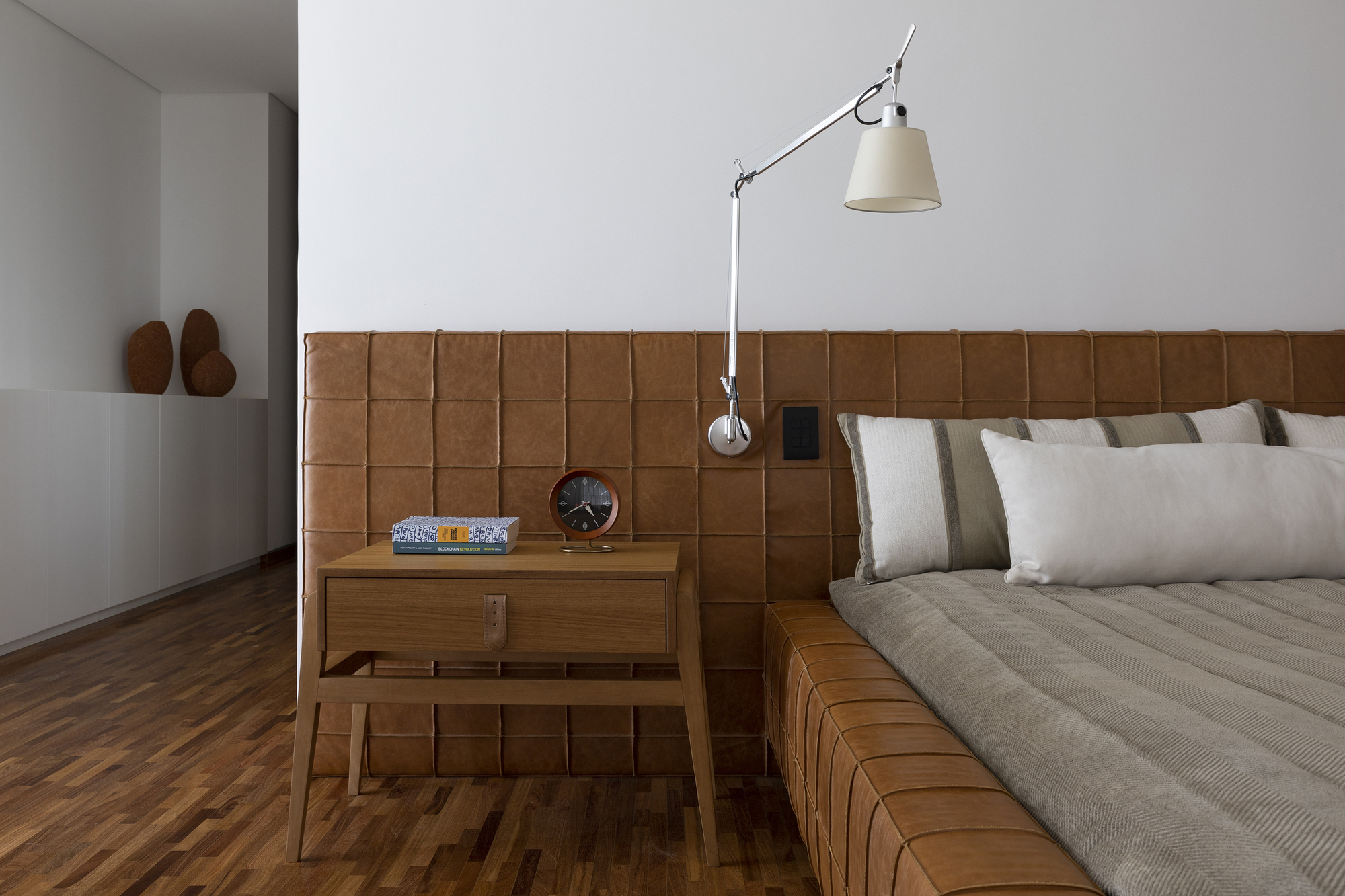 Close-up of the stitched leather headboard with swing-arm wall lamp and timber nightstand