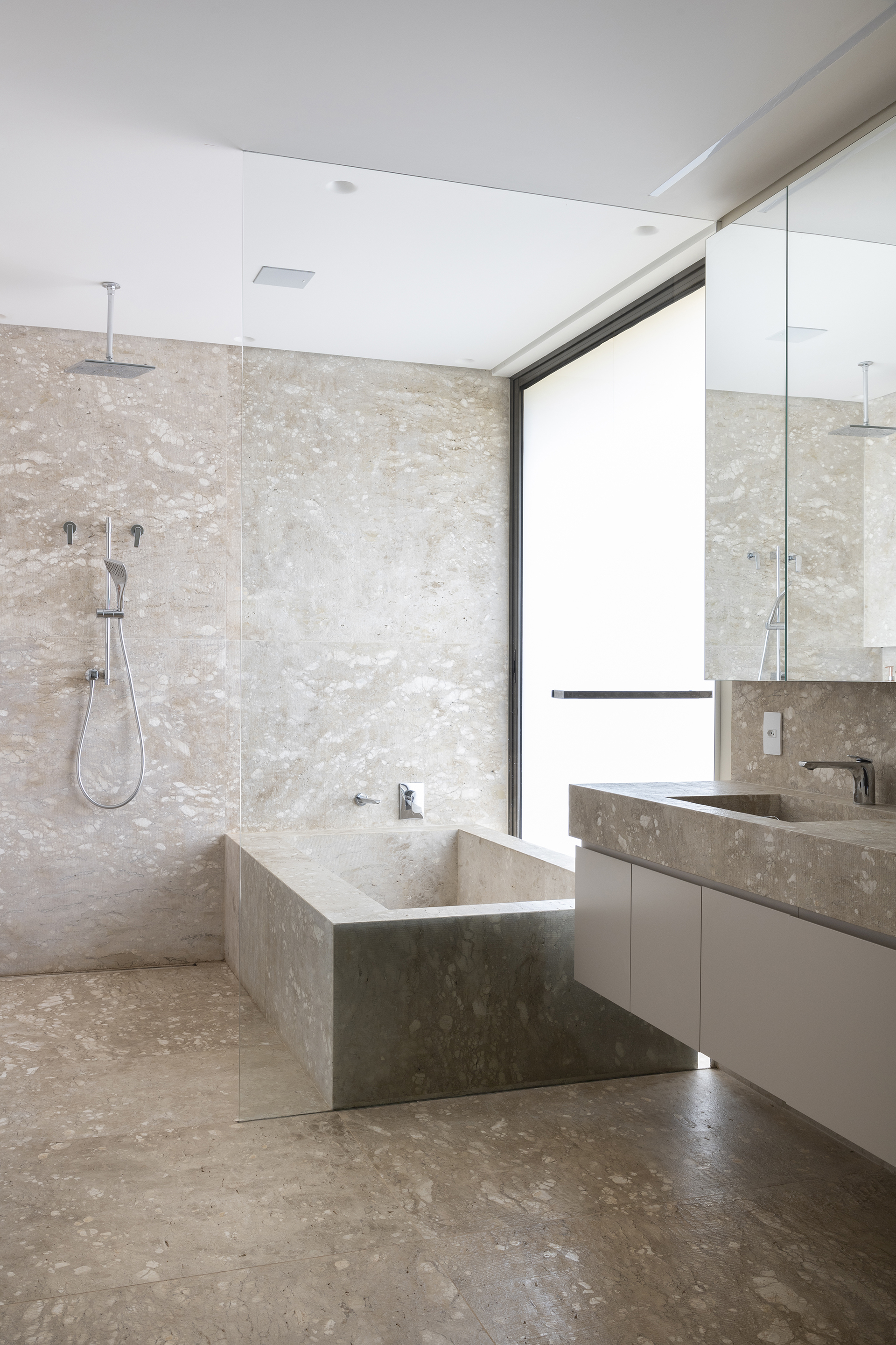 Travertine bathroom with freestanding angular tub beneath a frameless glass shower partition