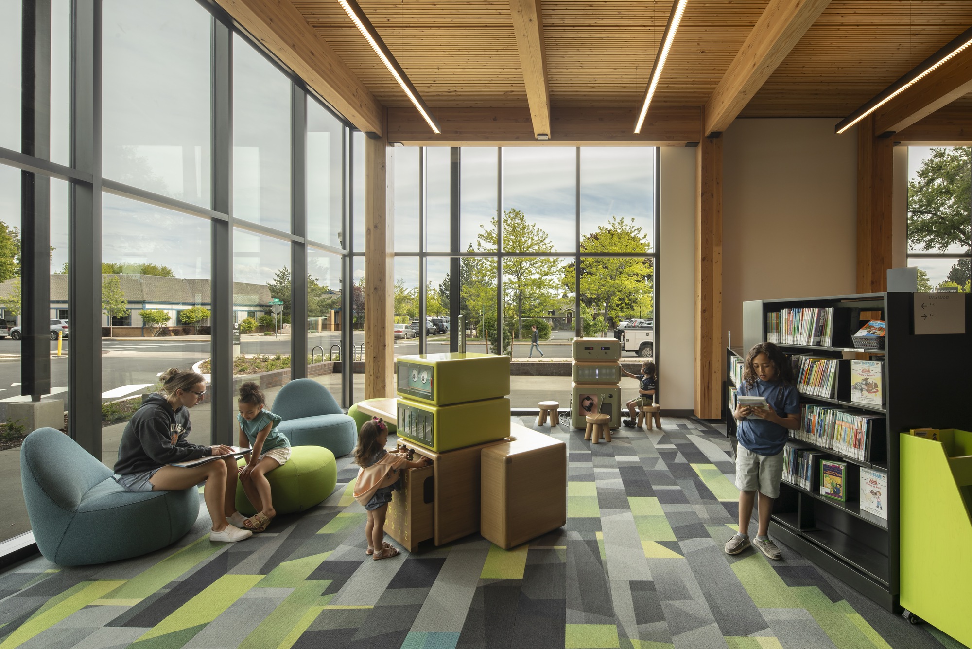 Reading area with patterned carpet tiles and glulam timber ceiling beams beneath tall glazed walls