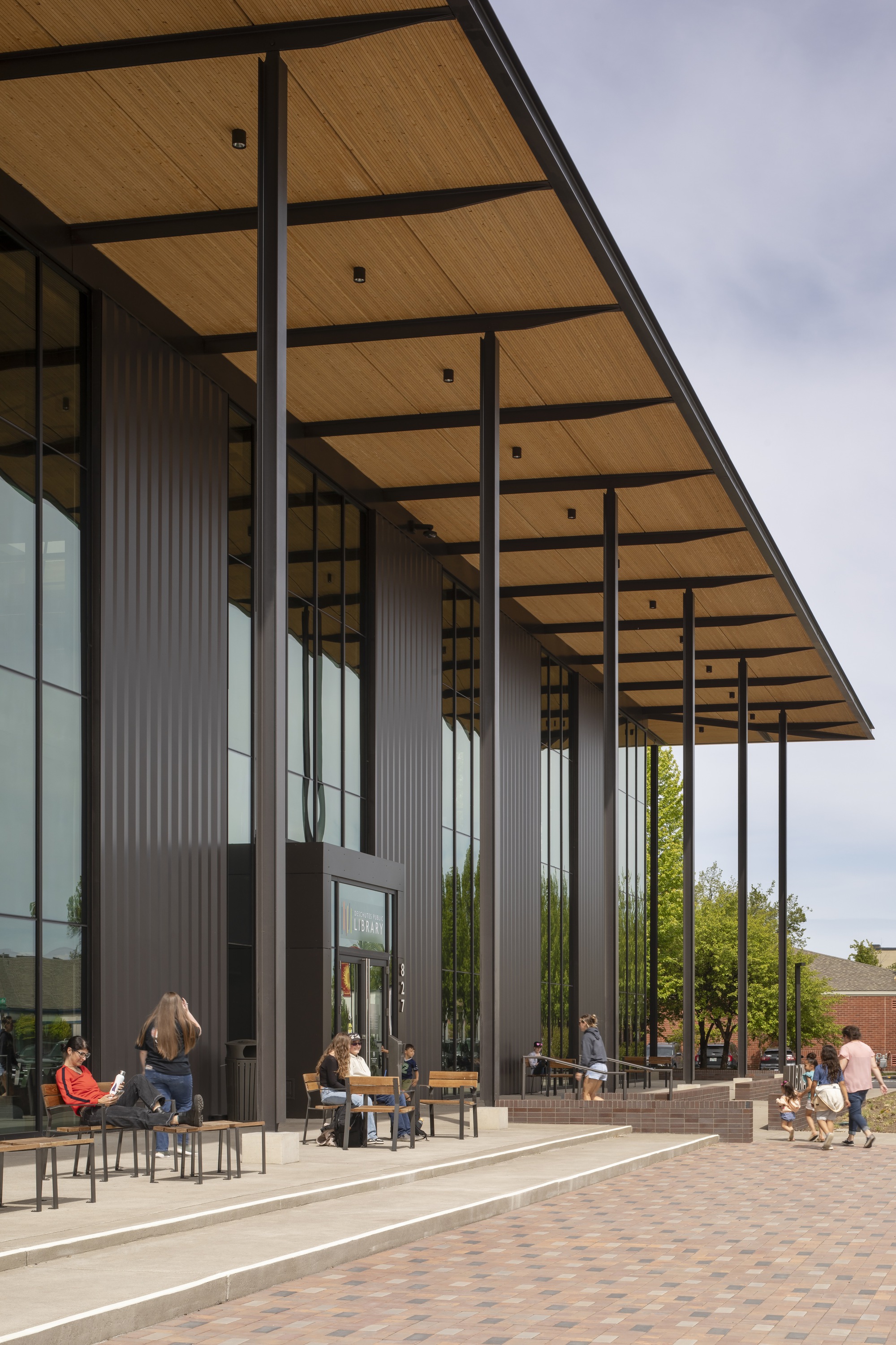 Covered entry plaza with slender steel columns supporting the timber-lined canopy above seated visitors