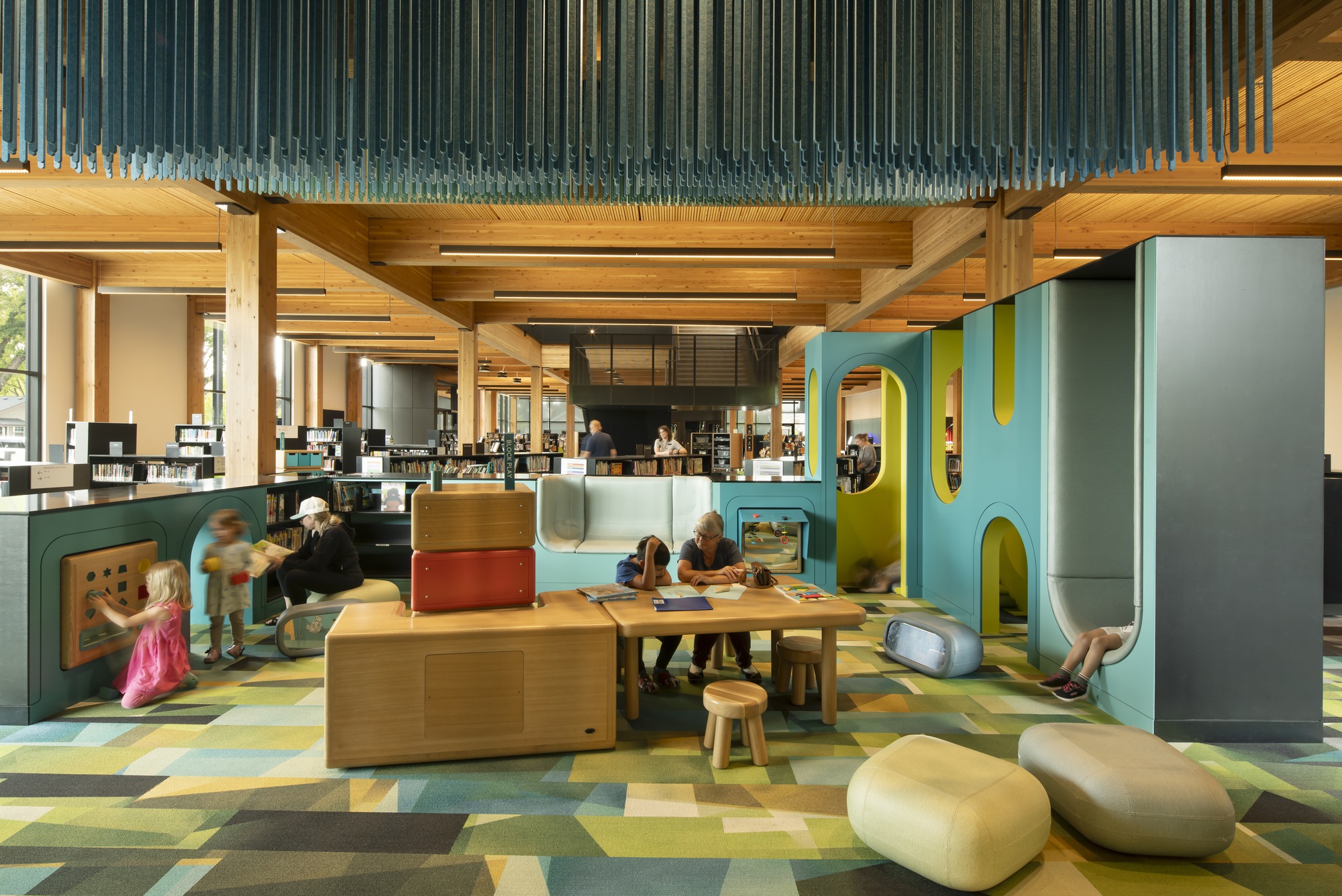 Children's area with vertical glass rod installation overhead, timber play structures and patterned floor tiles in daylight
