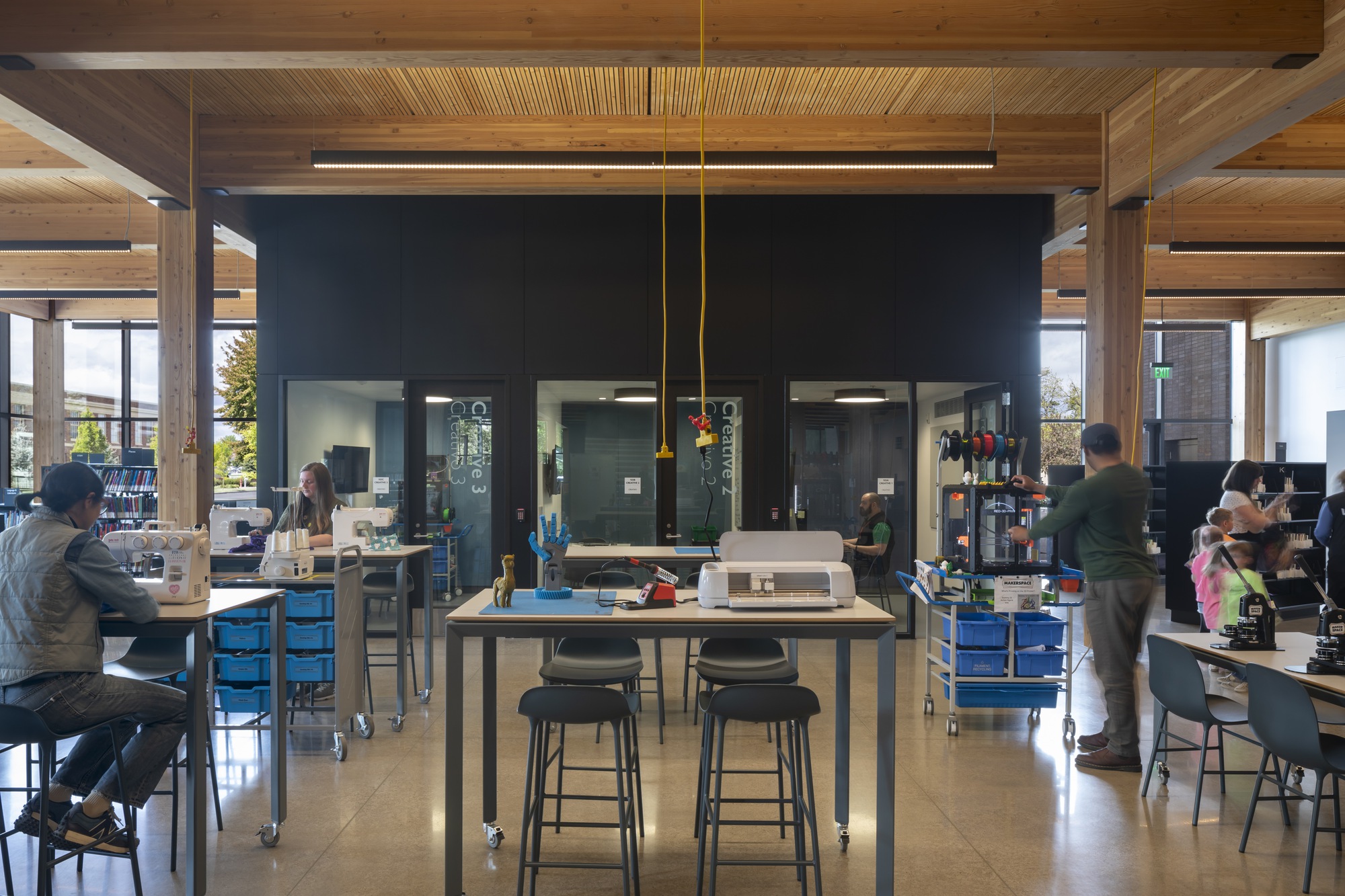 Workshop space with central table, black metal core volume and timber post-and-beam structure under natural light