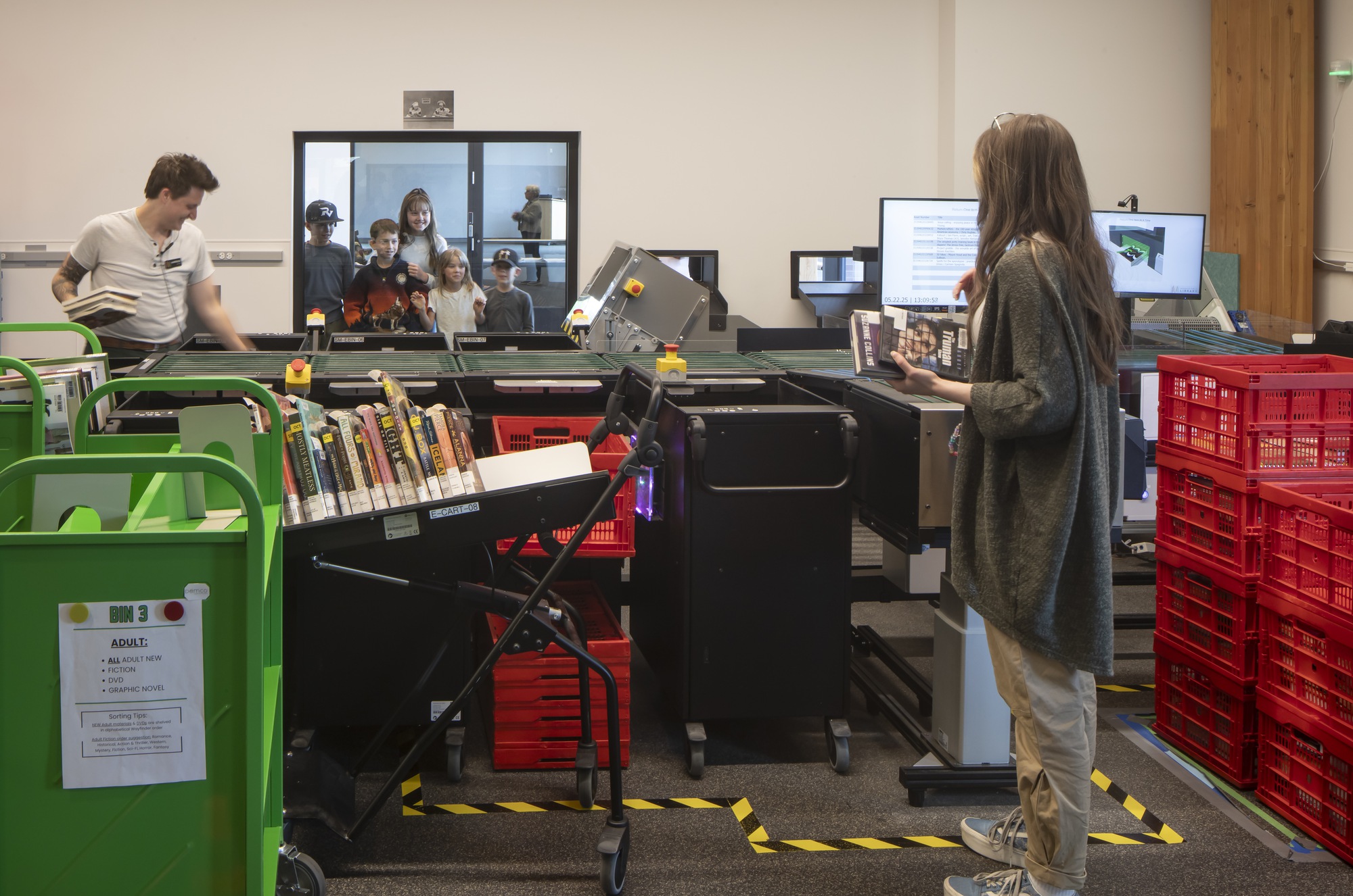 Book sorting workspace with automated conveyor system and colored bins behind a glass partition