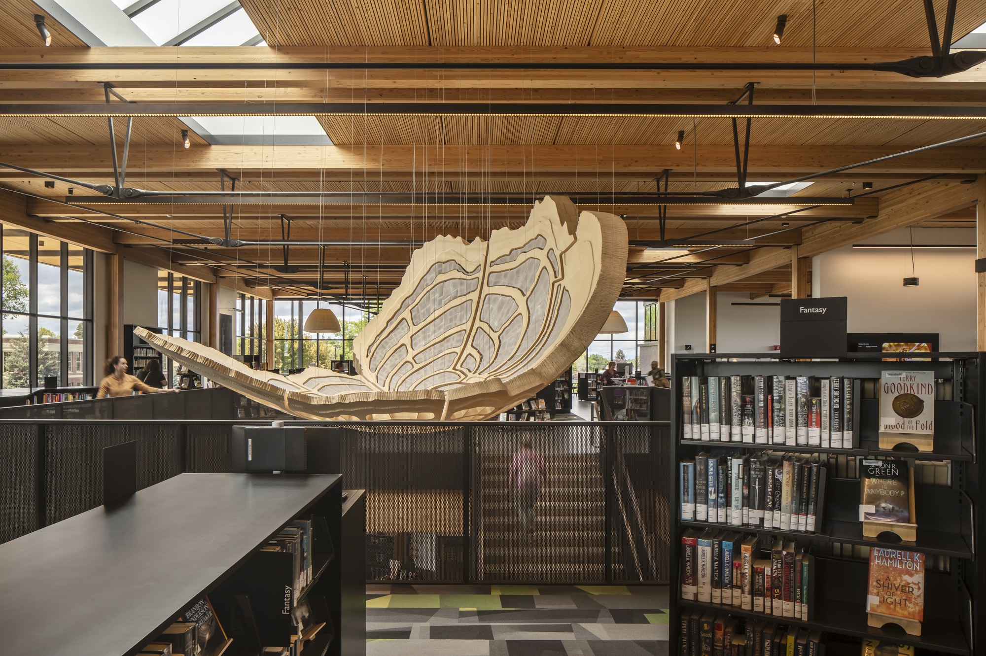 Laminated timber sculpture hanging above the main staircase with exposed wooden ceiling beams and skylights overhead