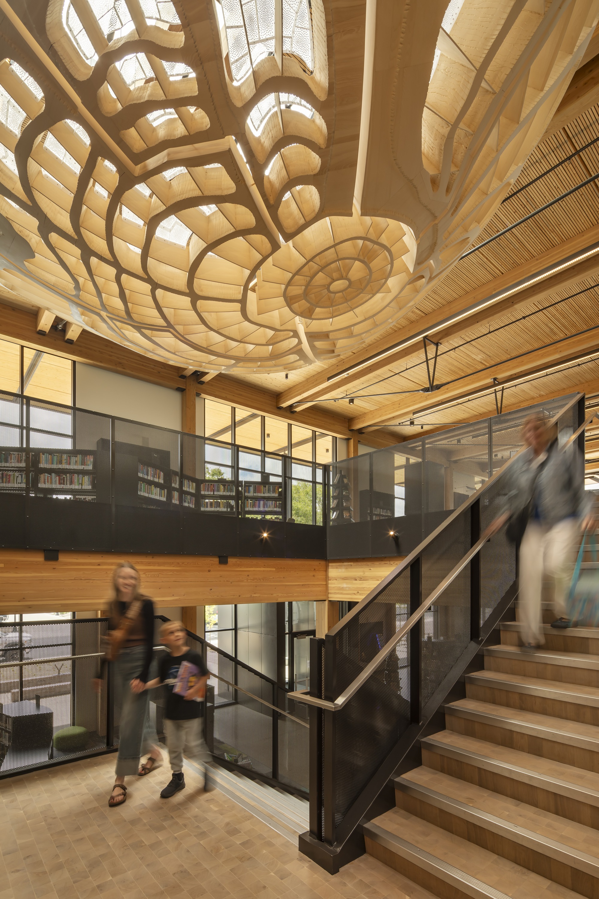 Double-height atrium with sculptural timber ceiling ribs and visitors ascending the wooden staircase