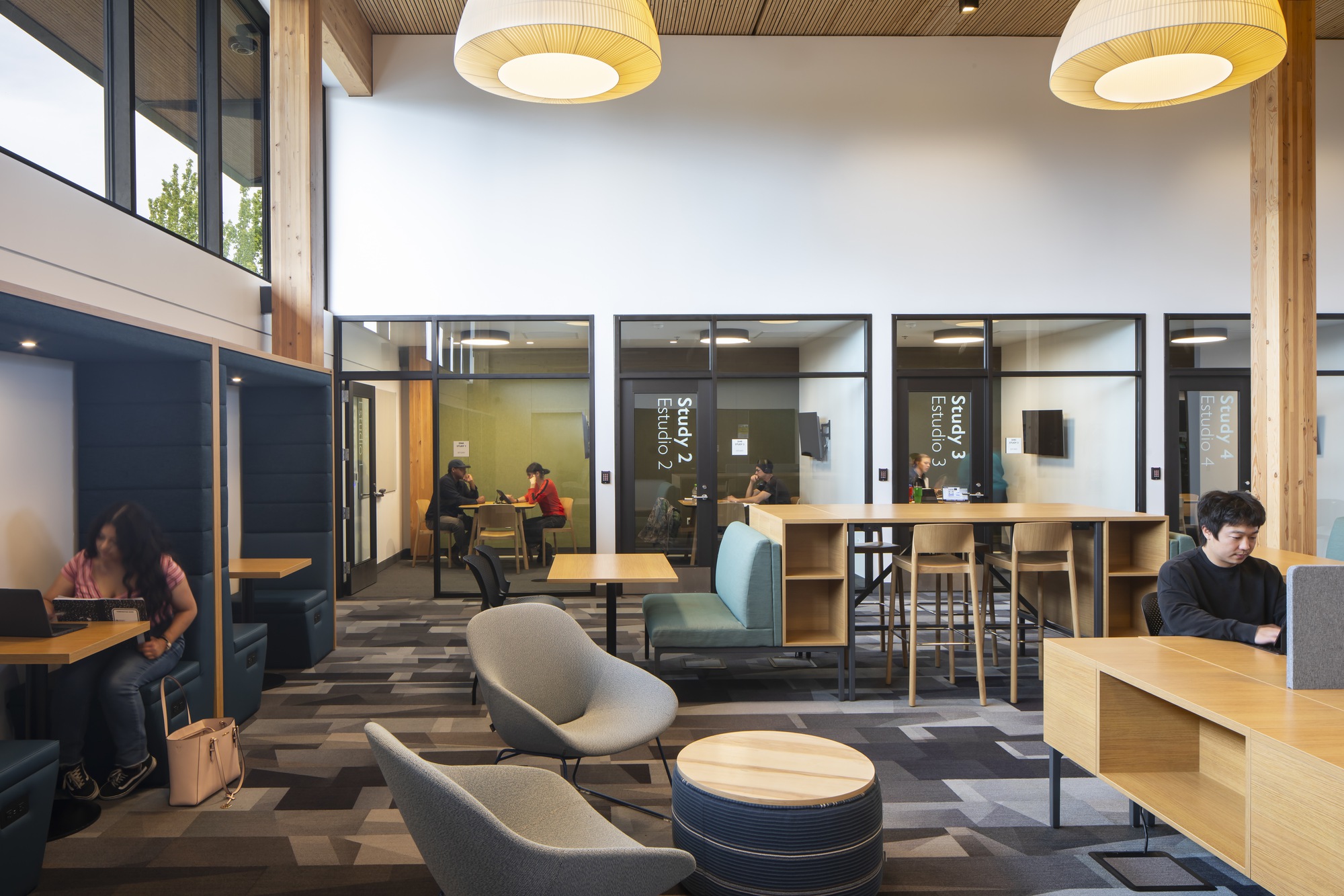 Reading area with glass-walled study rooms and visitors seated at tables under pendant lights