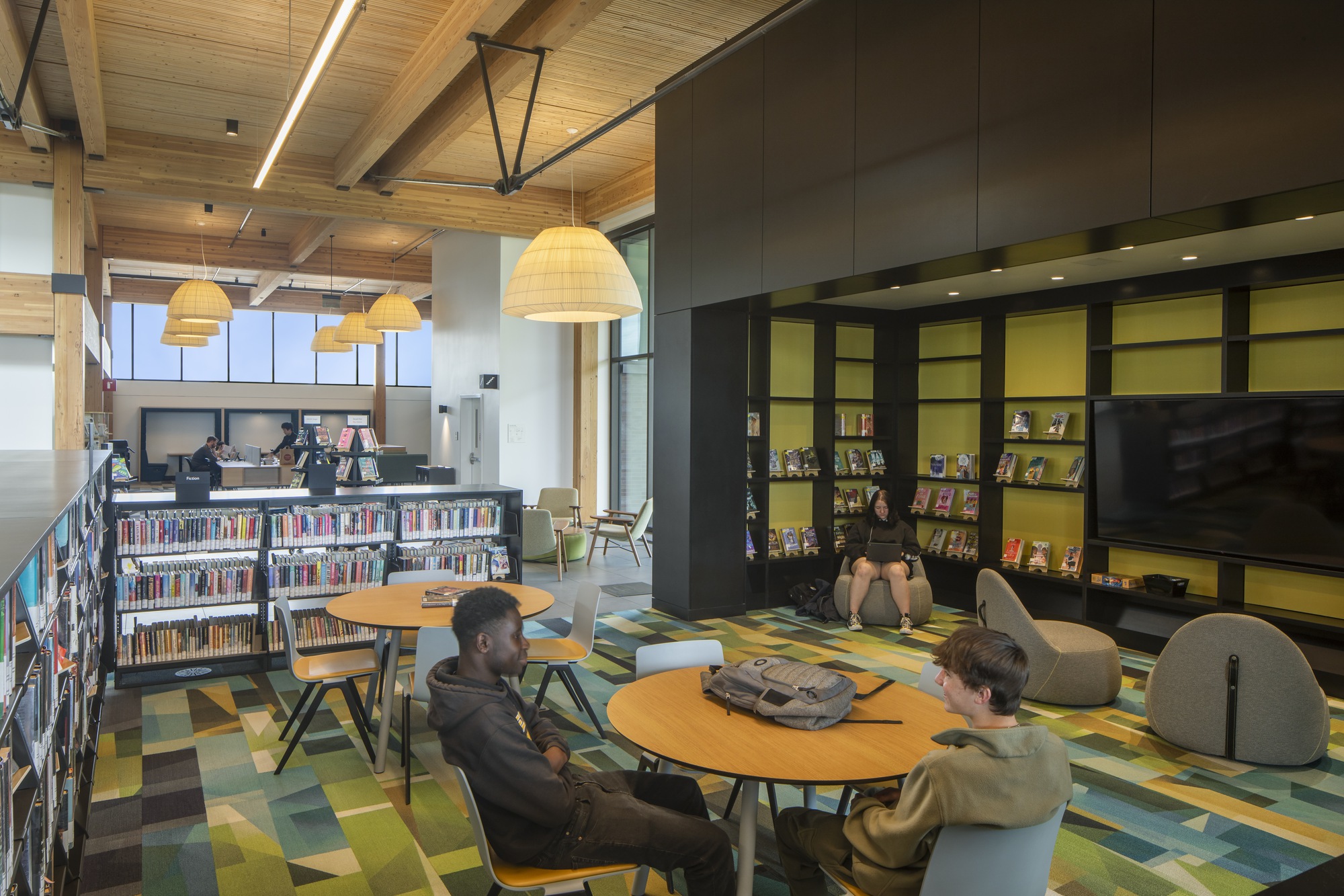 Reading area with round tables and pendant lights under a timber ceiling with two patrons conversing