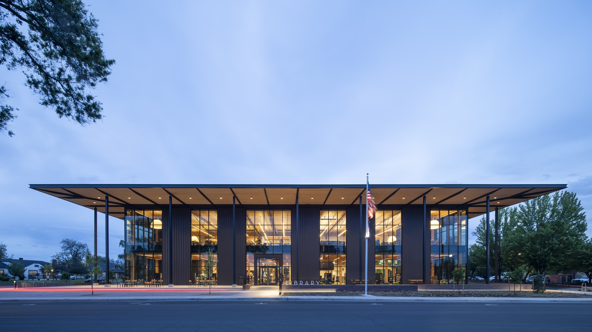 Street view of the glass and steel facade with deep roof overhang at dusk