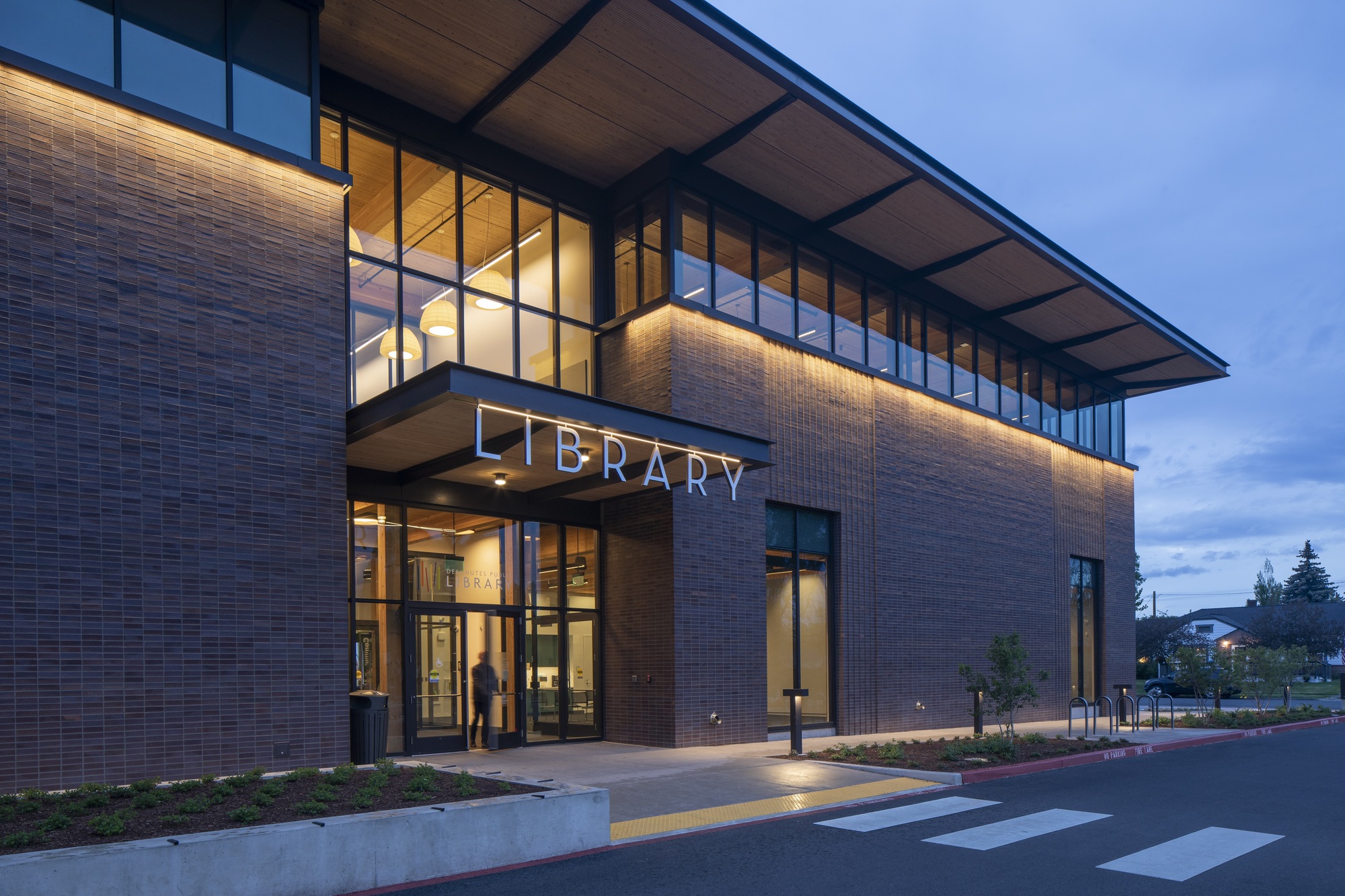 Entry canopy with glazed walls and illuminated brick facade at twilight with figure departing