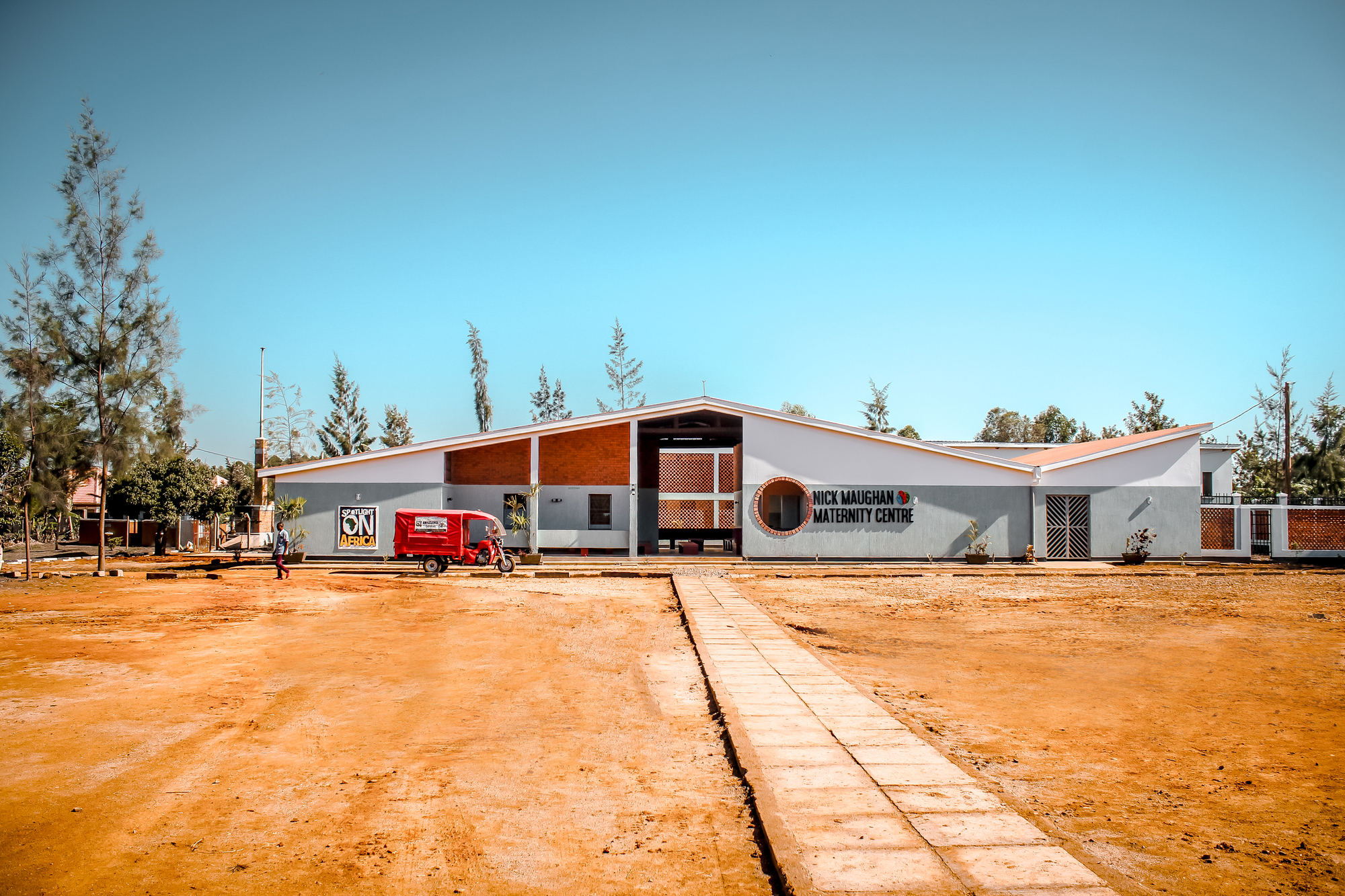 Frontal view showing the gabled roof forms with perforated screens and a concrete pathway across the compound