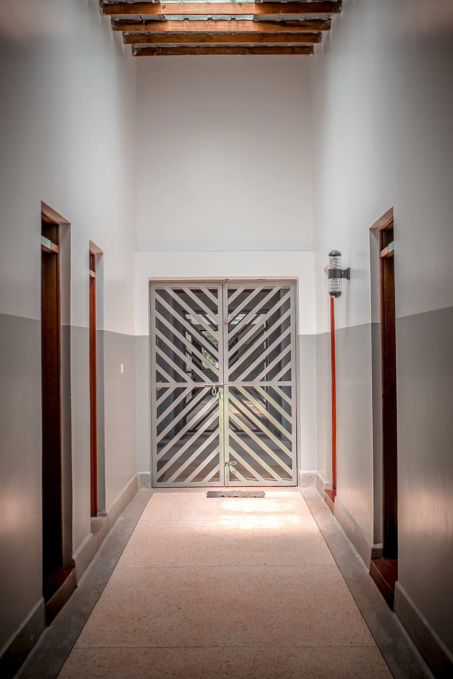 Corridor view toward double doors with diagonal timber slat pattern and exposed roof beams overhead